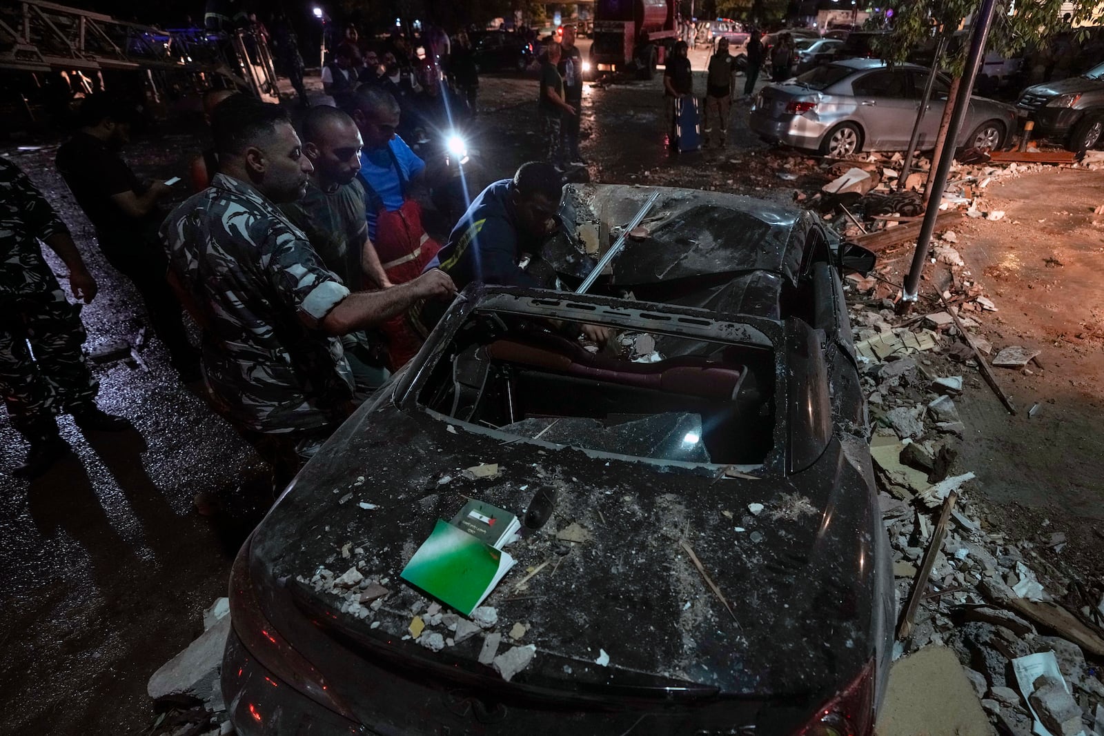 Policemen and civil defense workers inspect a damaged car near a building that was hit in an Israeli airstrike, in Beirut, Lebanon, early Monday, Sept. 30, 2024. (AP Photo/Bilal Hussein)