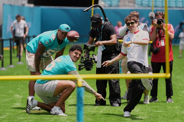 Ferrari driver Charles Leclerc of Monaco, right, kicks a ball as he tries out kicking football field goals with Miami Dolphins linebackers Jaelan Phillips (15) and Quinton Bell (56), during a joint event ahead of the Formula One Miami Grand Prix auto race, Thursday, May 1, 2025, in Miami Gardens, Fla. (AP Photo/Rebecca Blackwell)