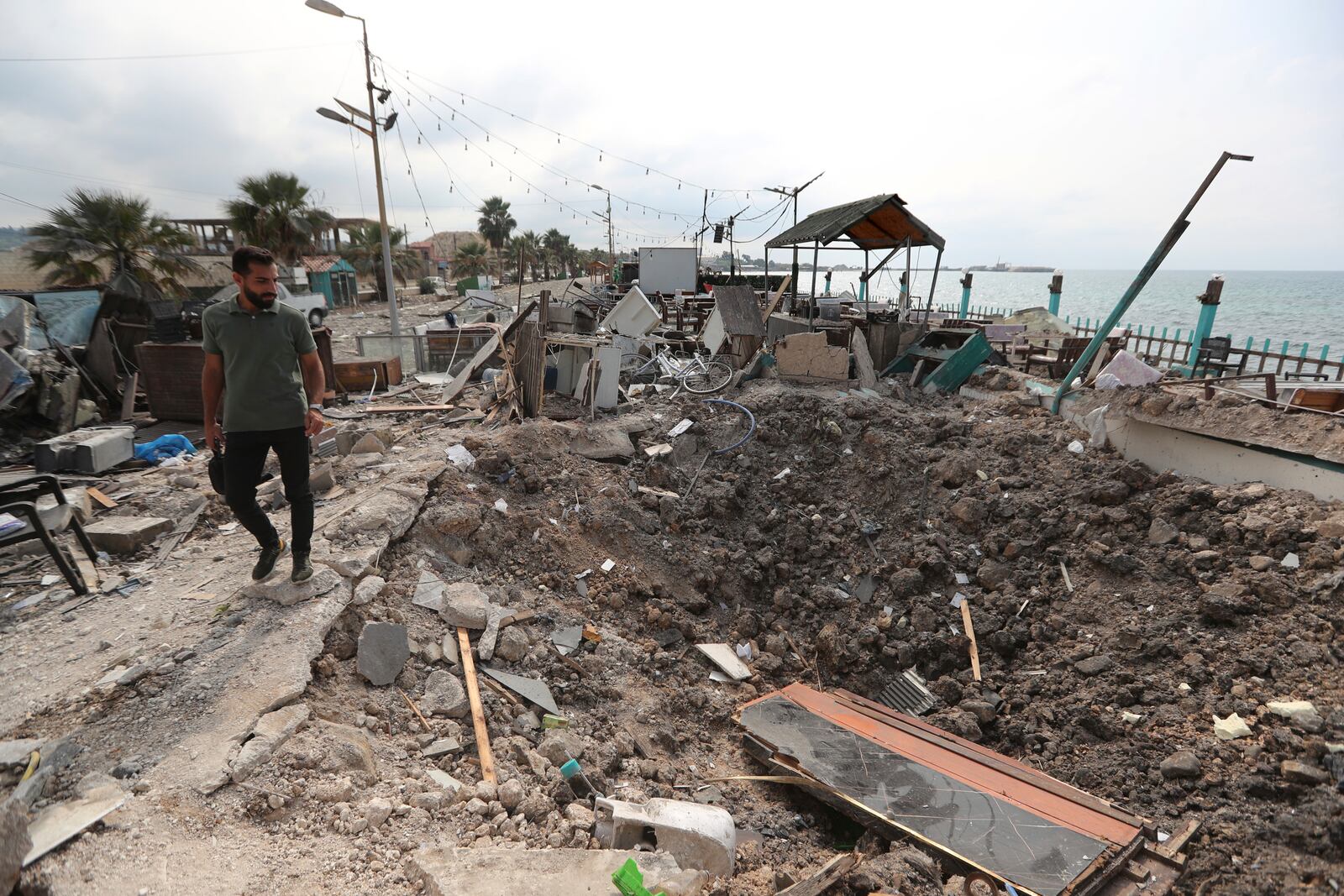 A man walks past a crater caused by an Israeli airstrike that hit a seaside coffee shop in Ghaziyeh town, south Lebanon, Sunday Oct. 6, 2024. (AP Photo/Mohammed Zaatari)