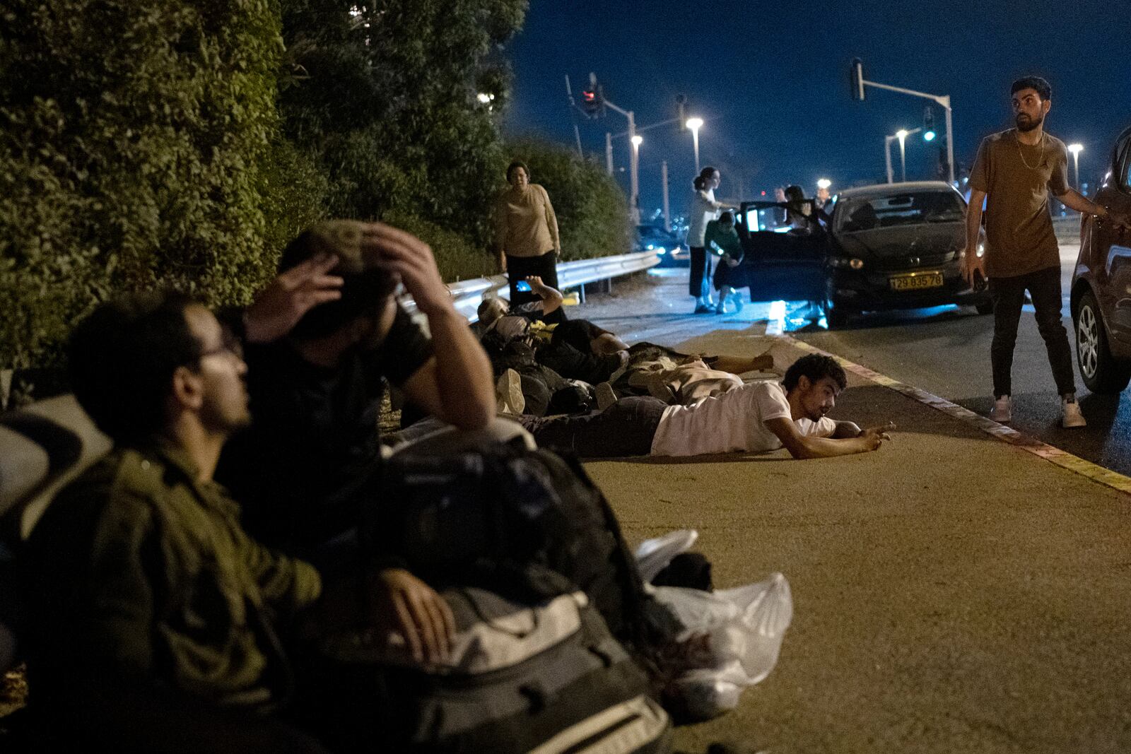 Israelis take cover as projectiles launched from Iran are being intercepted in the skies over in Rosh HaAyin, Israel, Tuesday, Oct. 1, 2024. (AP Photo/Maya Alleruzzo)