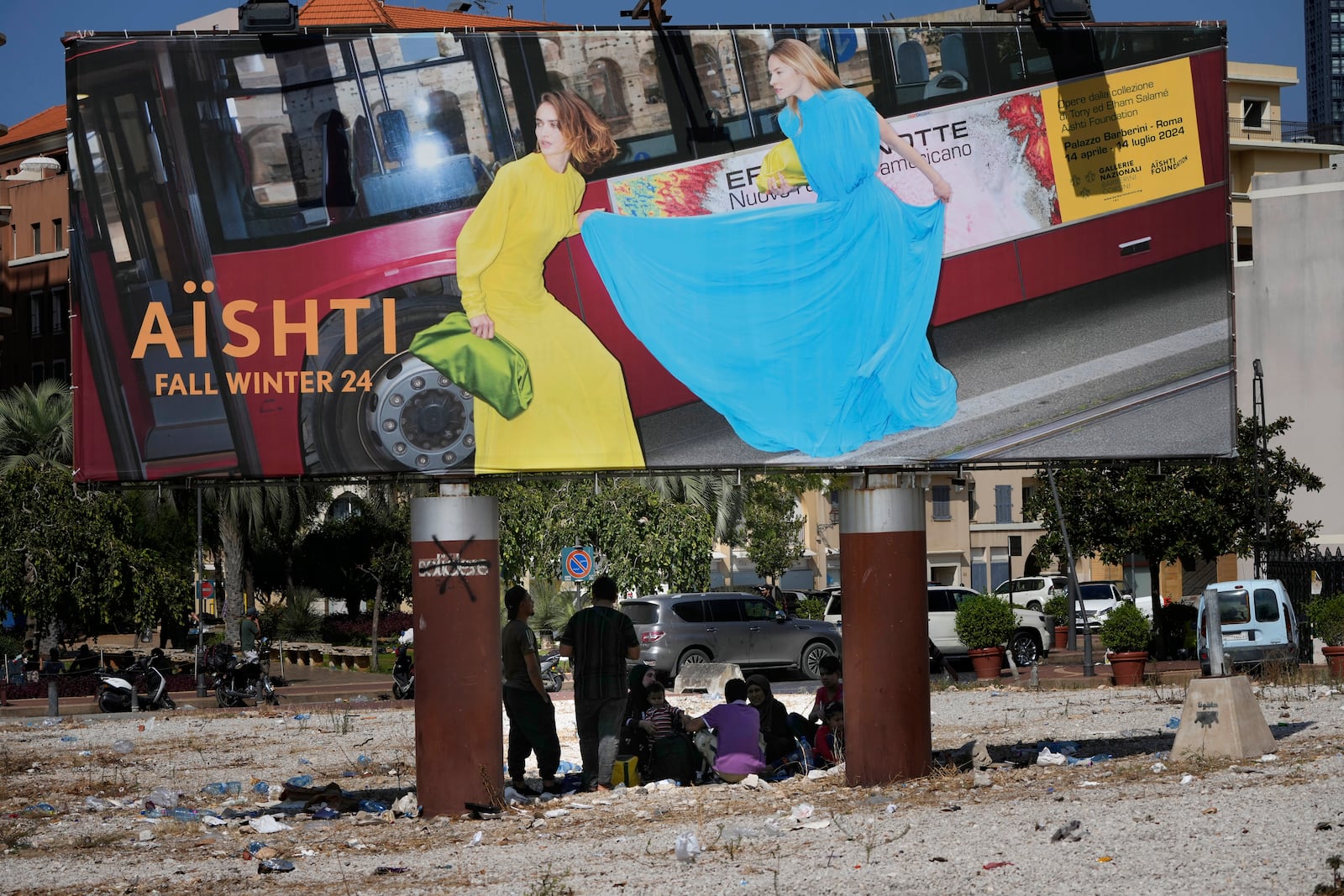 People who fled the southern suburb of Beirut amid ongoing Israeli airstrikes, take a shade under a billboard advertising fashion in downtown Beirut, Lebanon, Saturday, Sept. 28, 2024. (AP Photo/Hussein Malla)