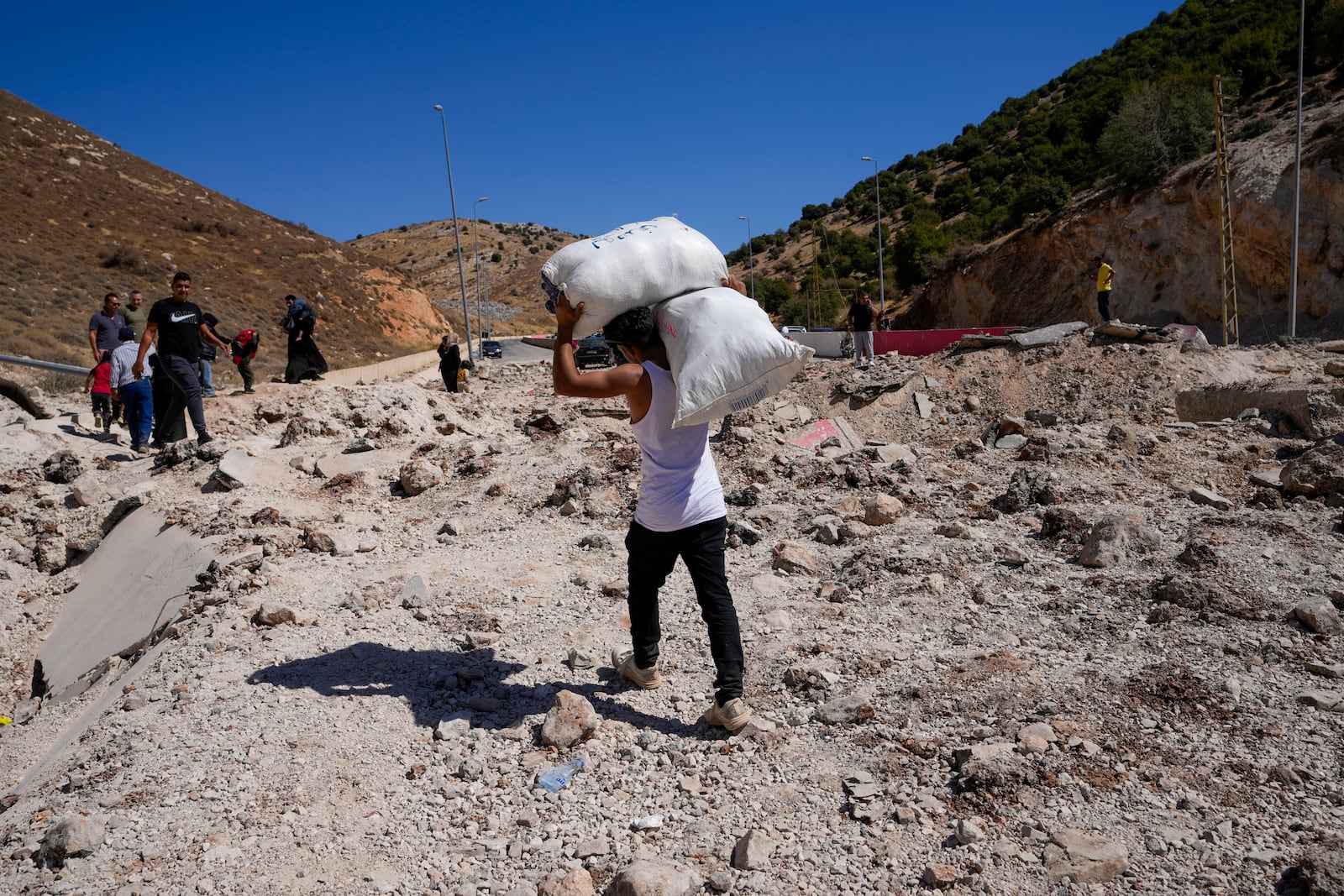 People carry their luggage as they cross into Syria on foot, through a crater caused by Israeli airstrikes aiming to block Beirut-Damascus highway at the Masnaa crossing, in the eastern Bekaa Valley, Lebanon, Saturday, Oct. 5, 2024. (AP Photo/Hassan Ammar)