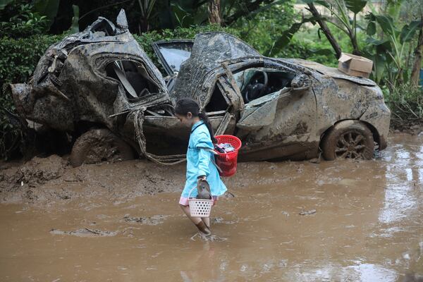 A young girl walks past the wreckage of a car after a landslide killed a number of people and left some others missing in Karo, North Sumatra, Indonesia, Monday, Nov. 25, 2024. (AP Photo/Binsar Bakkara)