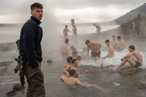 An Israeli soldier stands guard as residents and soldiers bathe in a hot water pool coming from a drilling project which exposed a subterranean hydrothermal spring near Mount Bental in the Israeli-controlled Golan Heights, on the first day of the ceasefire between Israel and Hezbollah, Wednesday, Nov. 27, 2024. (AP Photo/Ohad Zwigenberg)