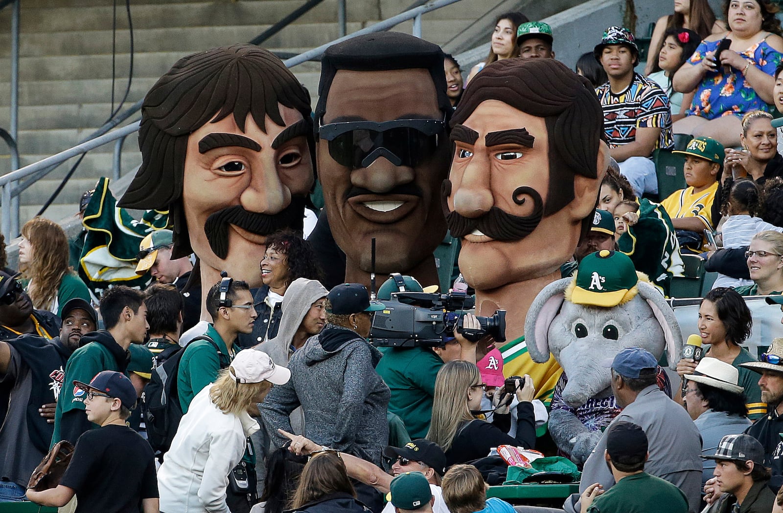 FILE - Contestants dressed as former Oakland Athletics players Dennis Eckersley, left, Rickey Henderson, center, and Rollie Fingers stand with fans after racing during the seventh inning of a baseball game between the Athletics and the Seattle Mariners in Oakland, Calif., July 3, 2015. (AP Photo/Jeff Chiu, File)