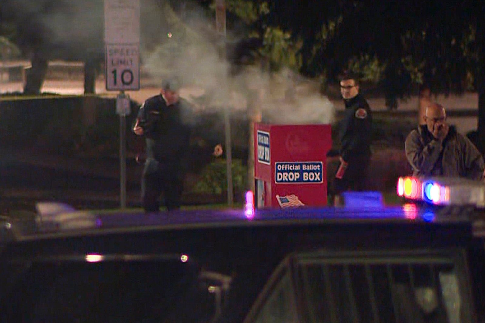 In this image made from a video provided by KGW8, authorities investigate smoke pouring out of a ballot box on Monday, Oct. 28, 2024, in Vancouver, Wash. (KGW8 via AP)