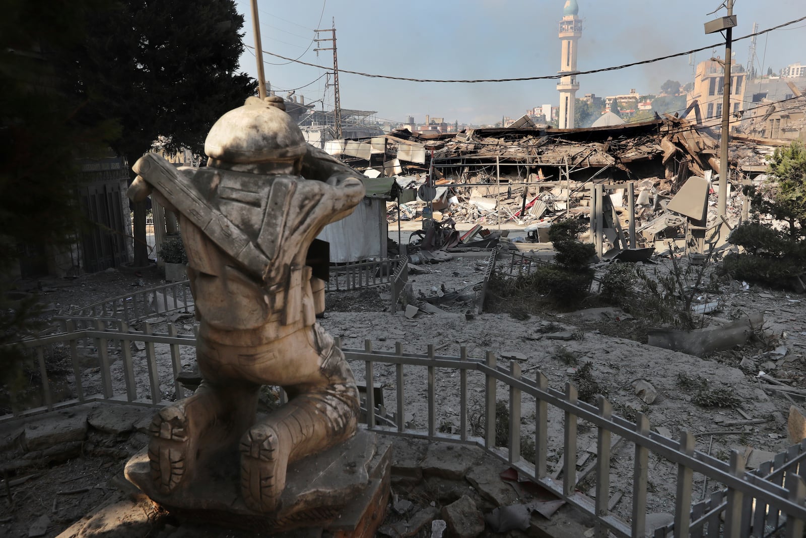 Destroyed shops are seen in front of a Hezbollah fighter statue on a commercial street that was hit Saturday night by Israeli airstrikes, in NAbatiyeh town, south Lebanon, Sunday, Oct. 13, 2024. (AP Photo/Mohammed Zaatari)