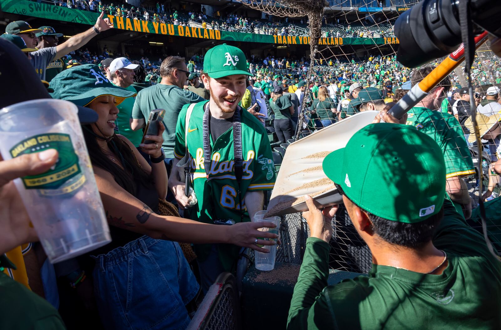 Grounds crew member Kyle Yamashita, front right, pours dirt from the field into containers for fans from a shovel after the Oakland Athletics defeated the Texas Rangers in a baseball game at the Coliseum in Oakland, Calif., Thursday, Sept. 26, 2024. It was the Athletics final home game at the Coliseum. (Carlos Avila Gonzalez/San Francisco Chronicle via AP)