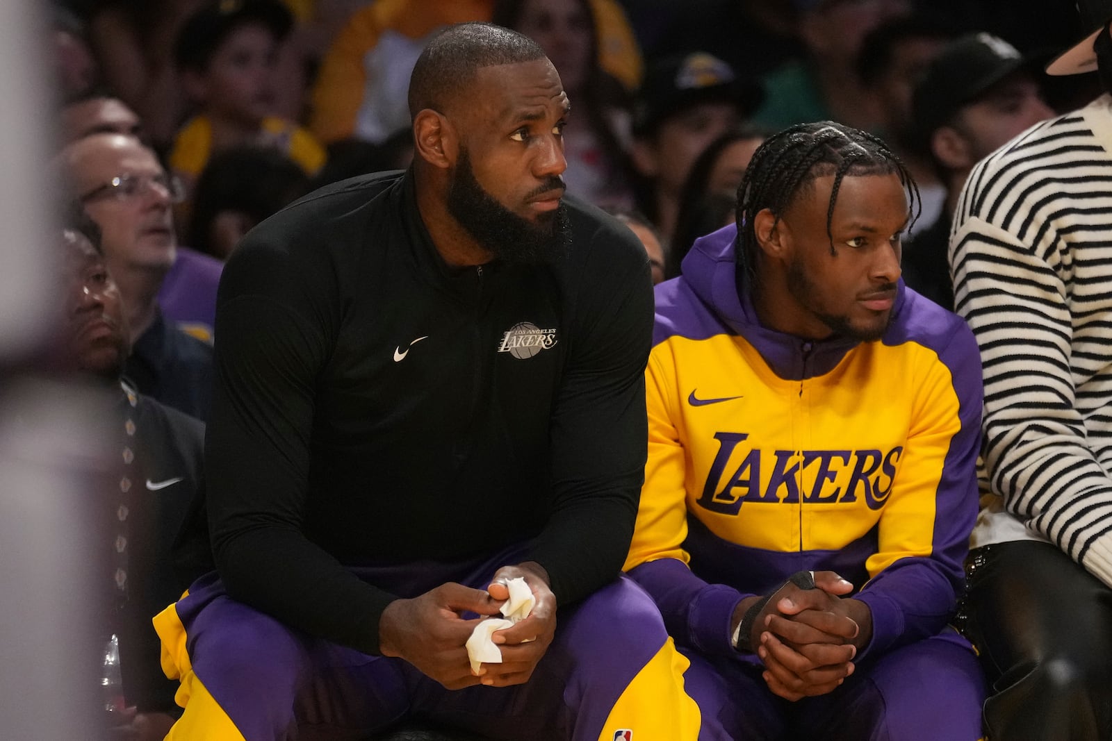 Los Angeles Lakers forward LeBron James guard Bronny James watch play during the first half of an NBA basketball game against the Minnesota Timberwolves, Tuesday, Oct. 22, 2024, in Los Angeles. (AP Photo/Eric Thayer)