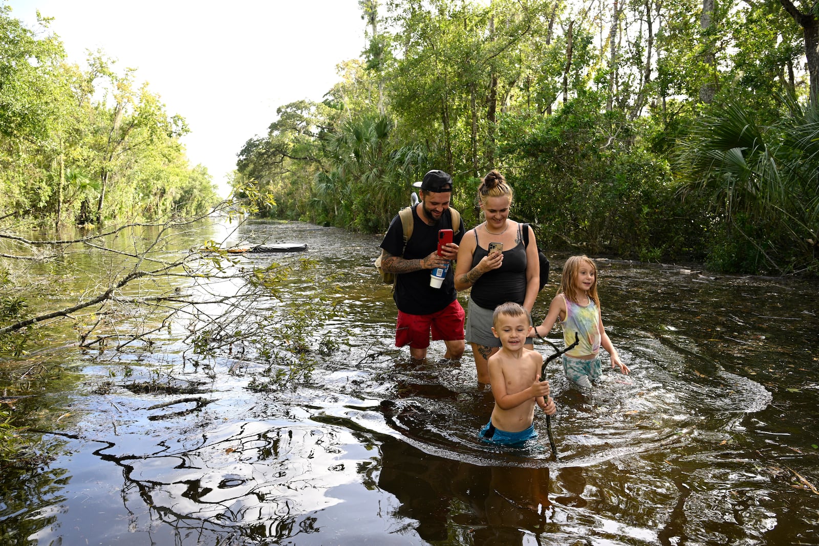 Dustin Holmes, rear left, his girlfriend Hailey Morgan, and her children Aria Skye Hall, 7, right, and Kyle Ross, 4, walk through a flooded road while returning to their home after Hurricane Helene passed near the area, Friday, Sept. 27, 2024, in Crystal River, Fla. (AP Photo/Phelan M. Ebenhack)