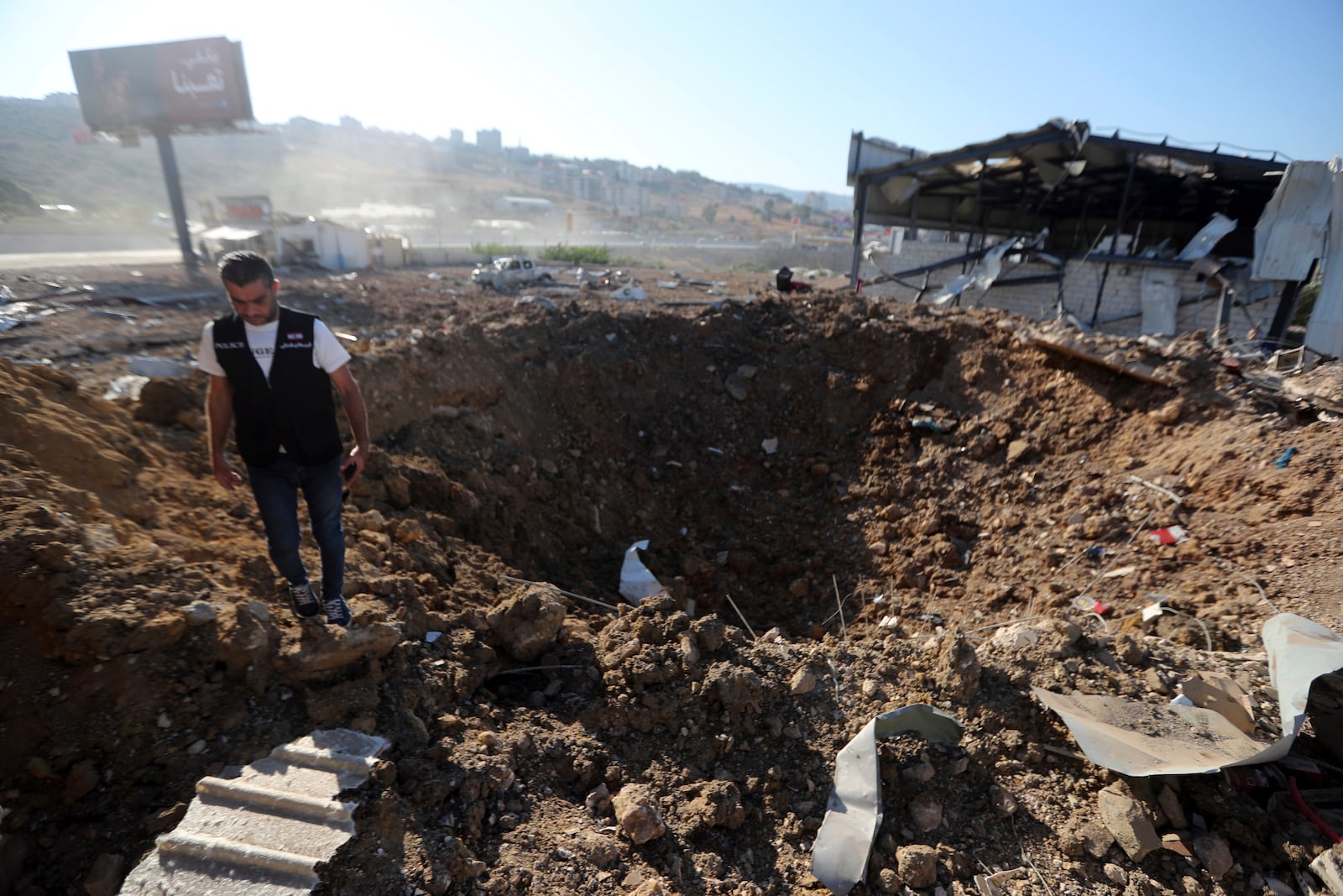 A Lebanese police intelligence stands near a crater at the site of an Israeli airstrike that hit a hangar in the southern town of Jiyeh, Lebanon, Wednesday, Sept. 25, 2024. (AP Photo/Mohammed Zaatari)