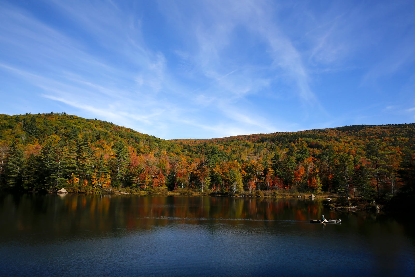 A fly fisherman paddles on a pond as fall foliage begins to show color in Campton, N.H., Sunday, Oct. 6, 2024. (AP Photo/Caleb Jones)