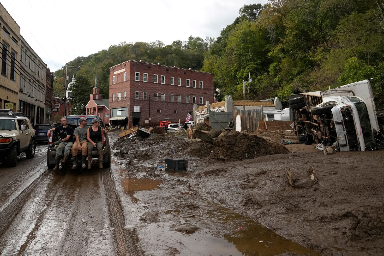 People ride in the back of a pickup truck on a mud-covered street left in the aftermath of Hurricane Helene, Tuesday, Oct. 1, 2024, in Marshall, N.C. (AP Photo/Jeff Roberson)