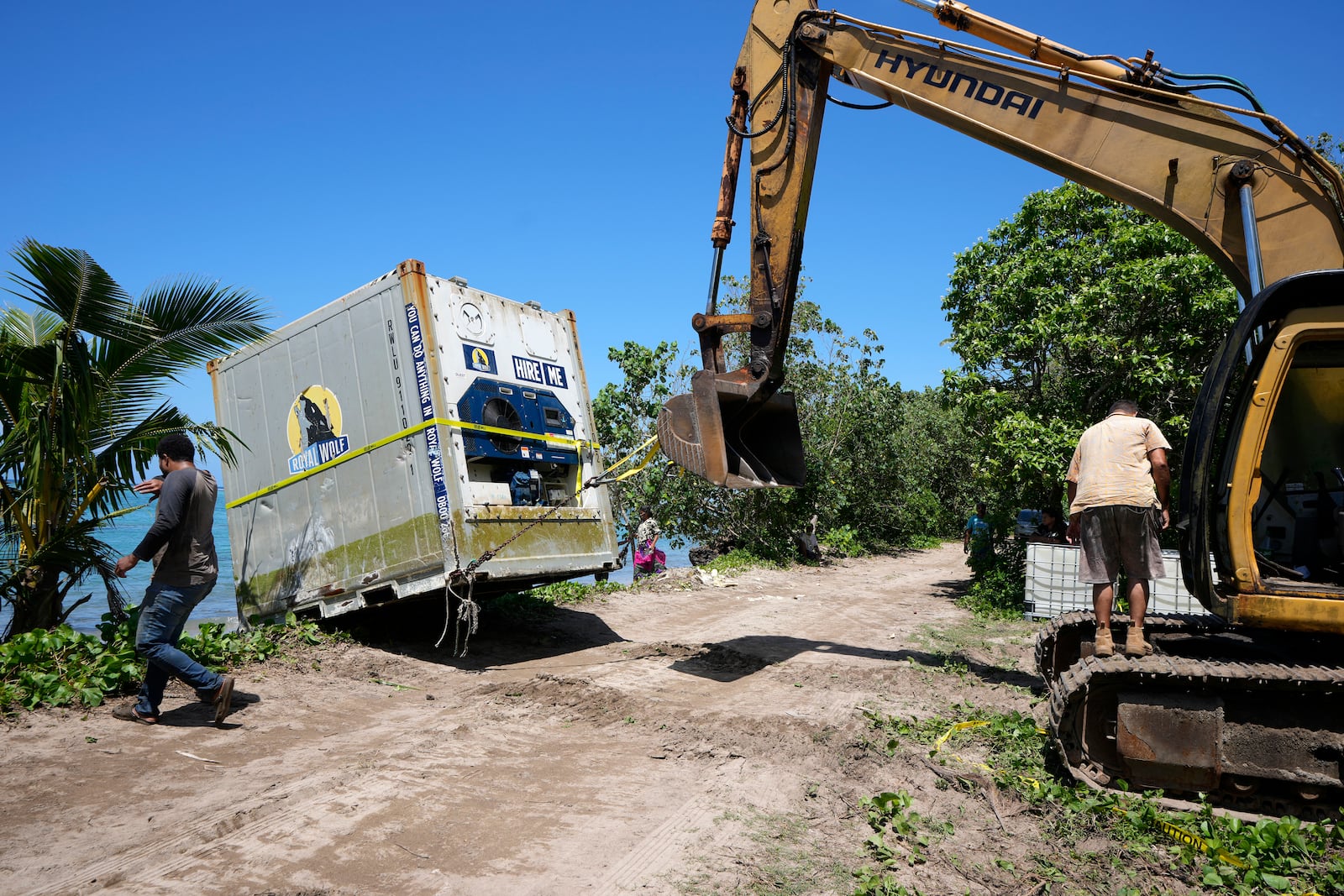 An excavator is used to drag a shipping container onto the beach in the village of Mulivai Safata, Samoa, on Monday, Oct. 21, 2024, near where a New Zealand navy ship ran aground and sank on Oct. 6. (AP Photo/Rick Rycroft)