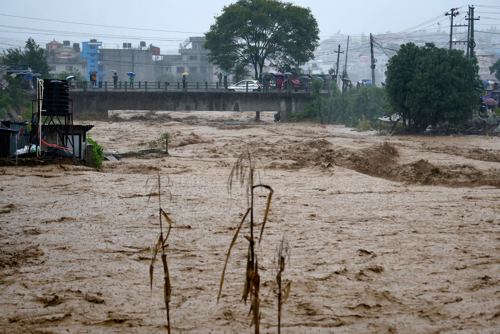 People watch the turbulent waters of Bagmati River from a bridge as the river flooded due to heavy rains in Kathmandu, Nepal, Saturday, Sept. 28, 2024. (AP Photo/Gopen Rai)