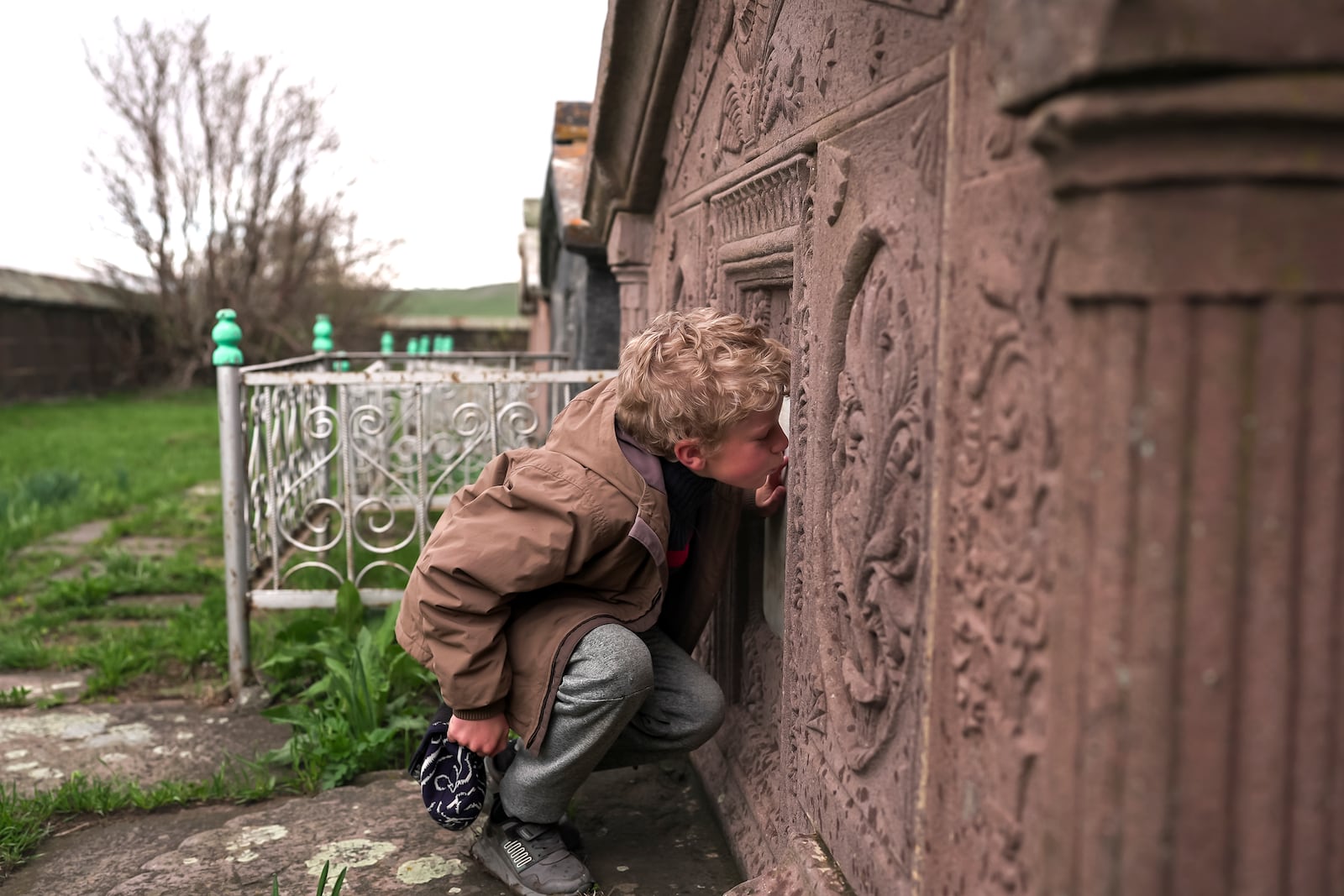 Ilya Strukov, 10, kisses a tombstone on a grave of his Doukhobor ancestors at a cemetery outside of the remote mountain village of Orlovka, Georgia, Sunday, May 5, 2024. (AP Photo/Kostya Manenkov)