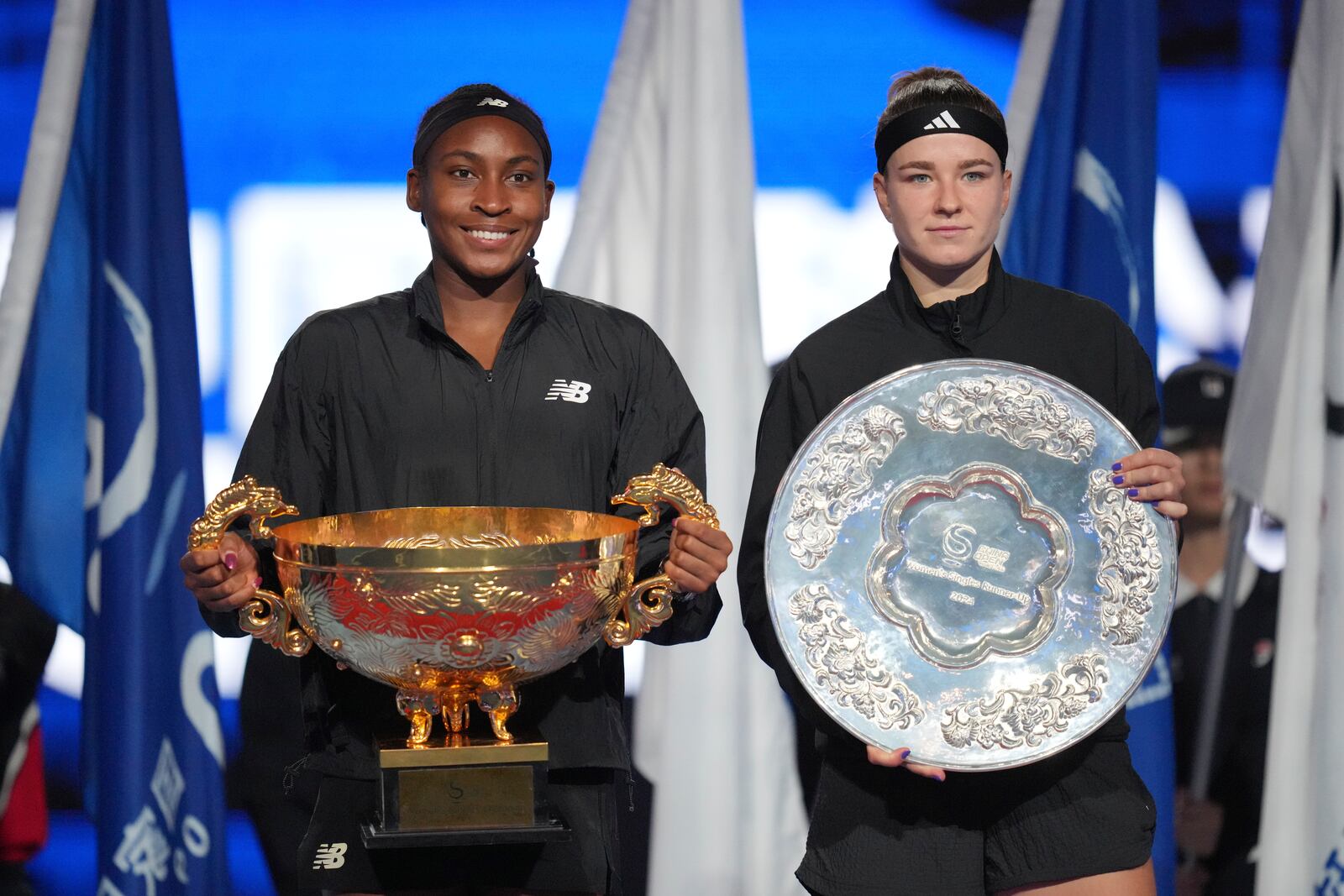 Coco Gauff of the United States, left, holds the championship trophy as she pose for photographers with Karolina Muchova of Czech Republic after defeating her in the women's singles final match at the China Open tennis tournament at the National Tennis Center in Beijing, Sunday, Oct. 6, 2024. (AP Photo/Achmad Ibrahim)