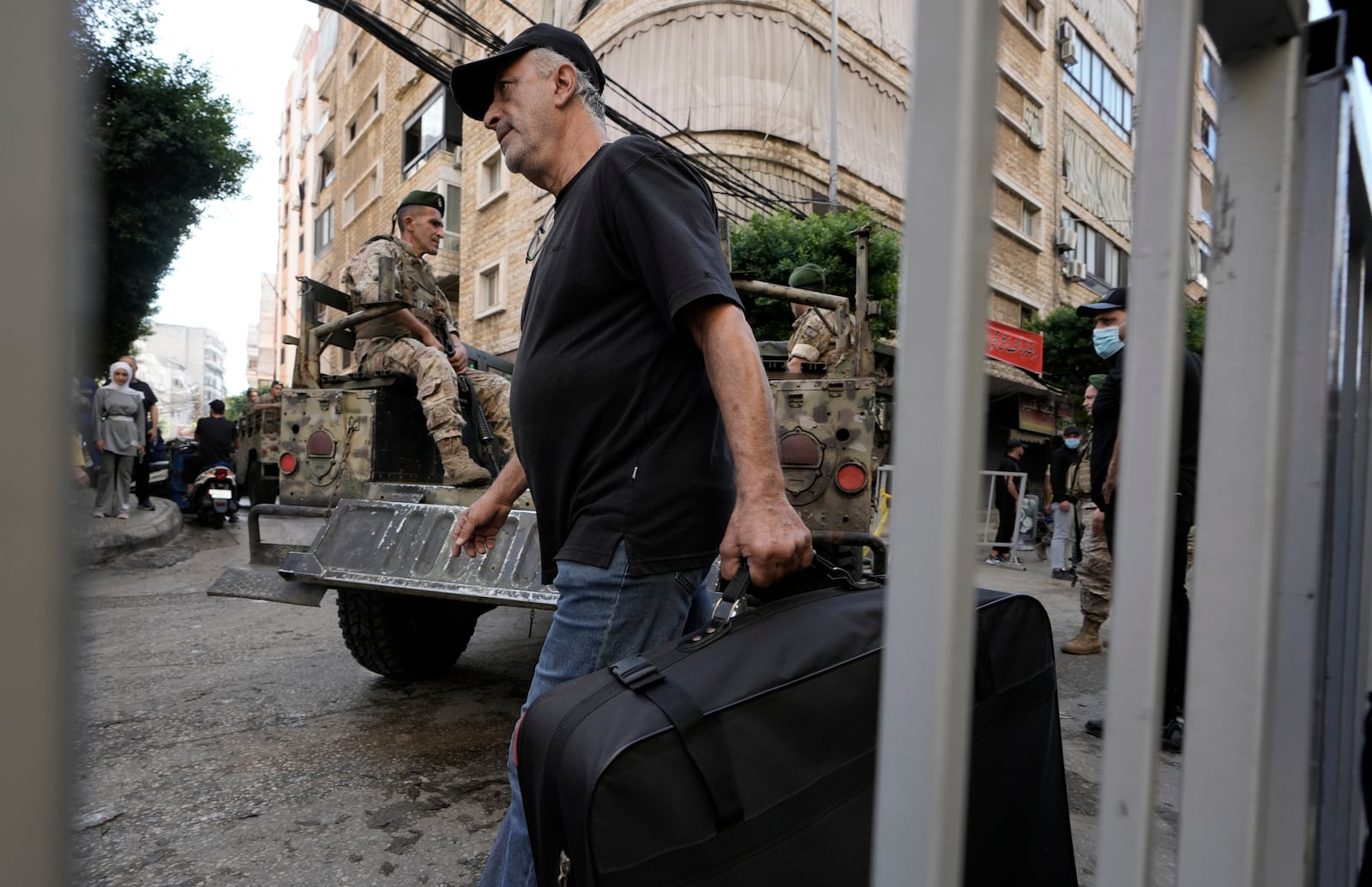 A man walks with a suitcase as Lebanese soldiers drive near the site of Friday's Israeli strike in Beirut's southern suburb, Sunday, Sept. 22, 2024. (AP Photo/Bilal Hussein)