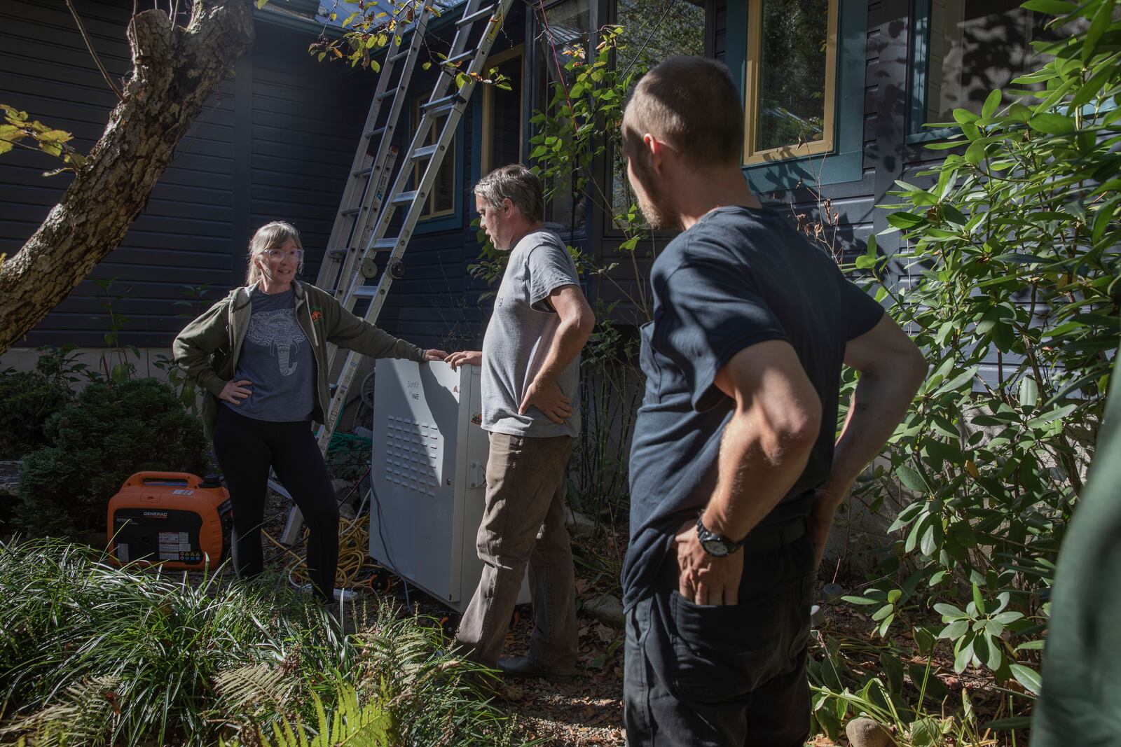 Julie Wiggins, left, talks with Hayden Wilson, center, and Henry Kovacs, right, about the mobile power system just delivered to her makeshift distribution hub in Bakersville, N.C. on Oct. 9, 2024. (AP Photo/Gabriela Aoun Angueria)