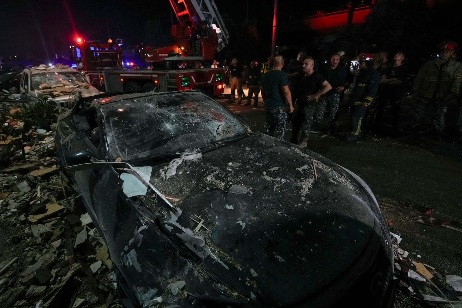 Policemen and civil defense workers stand next to damaged cars near a building that was hit in an Israeli airstrike, in Beirut, Lebanon, early Monday, Sept. 30, 2024. (AP Photo/Bilal Hussein)