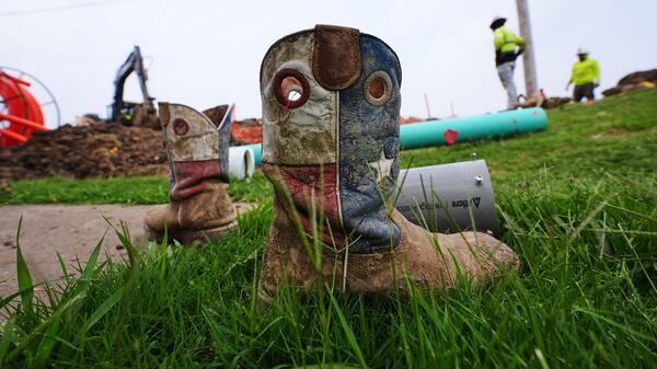 A worker's Texas themed boots sit in the grass as a crew works laying fiber optic cable in Princeton, Texas, Friday, May 16, 2025. (AP Photo/LM Otero)