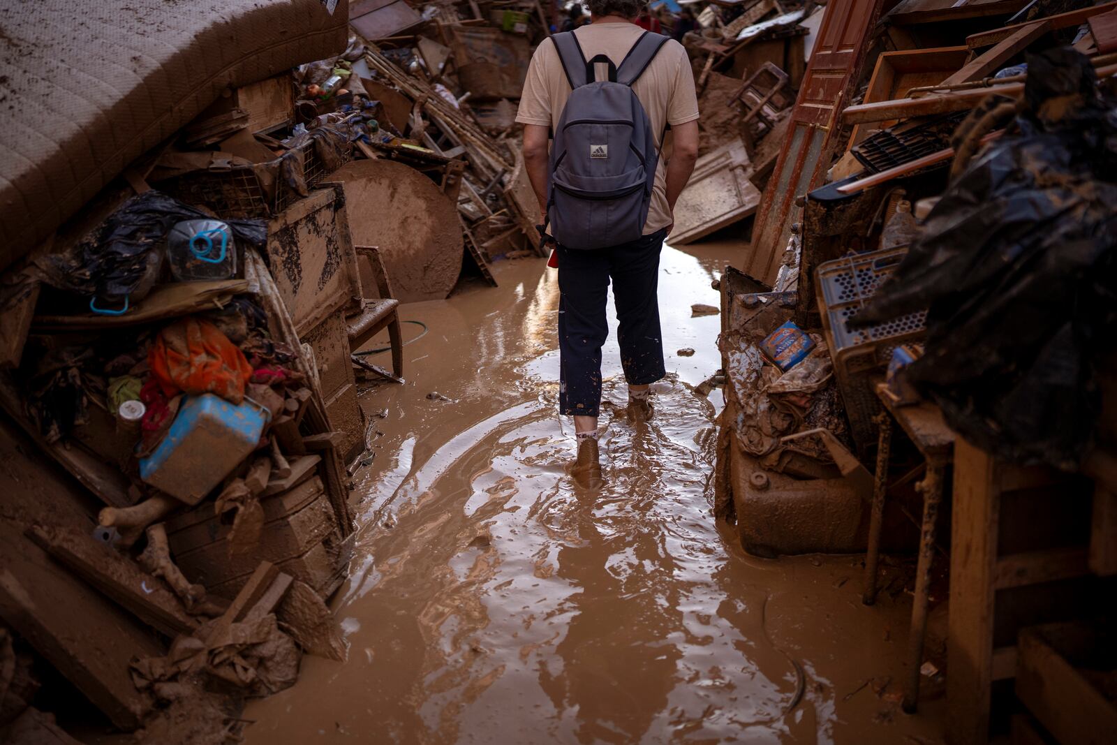 A person walks through a street with piled furniture and rubbish on the sides, in an area affected by floods in Paiporta, Valencia, Spain, Tuesday, Nov. 5, 2024. (AP Photo/Emilio Morenatti)