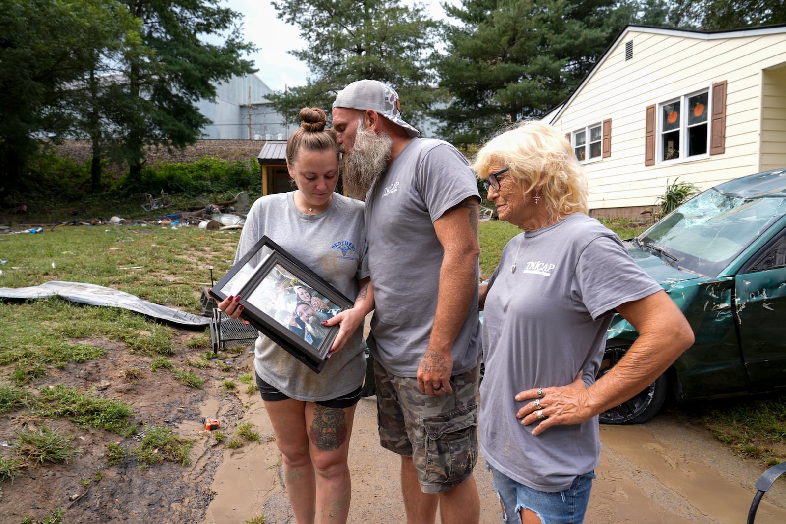 Dustin Bentley, center kisses his wife Jennifer Bentley, left, after retrieving family photos from their flood damaged home as his mother Janet Sams looks on Saturday, Sept. 28, 2024, in Newport, Tenn. (AP Photo/George Walker IV)