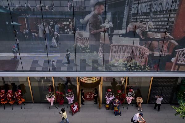 Workers wait for customer at a jewellry store as a projector screen promoting a newly opened outdoor Hutong style shopping mall, in Beijing, Monday, May 26, 2025. (AP Photo/Andy Wong)