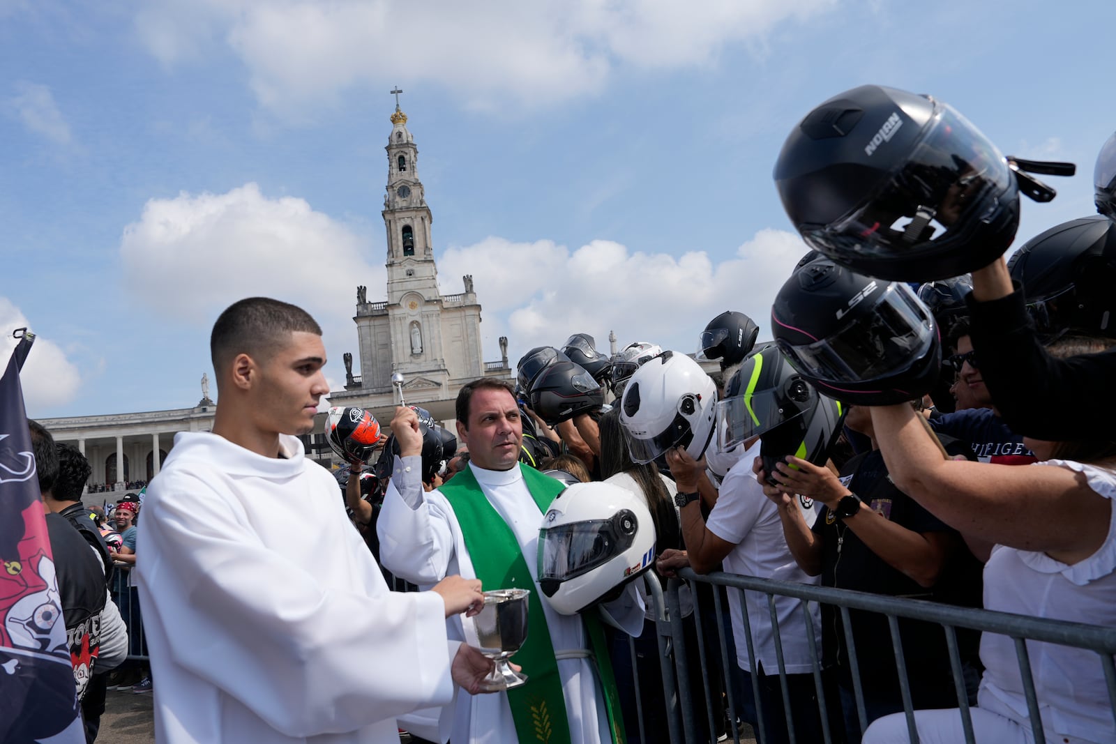 A priest holding a police motorcycling helmet, blesses the helmets of faithful during the IX Pilgrimage of the Blessing of Helmets that draws tens of thousands at the Roman Catholic holy shrine of Fatima, in Fatima, Portugal, Sunday, Sept. 22, 2024. (AP Photo/Ana Brigida)