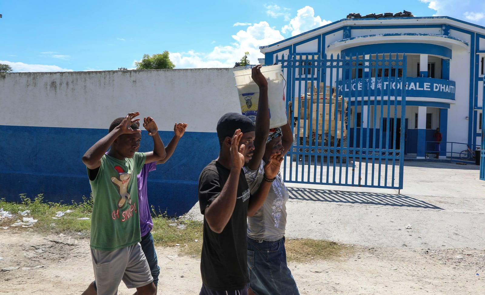 People raise their arms while walking past a police station in Pont-Sonde, Haiti, Monday, Oct. 7, 2024, days after a gang attacked the town. (AP Photo/Odelyn Joseph)