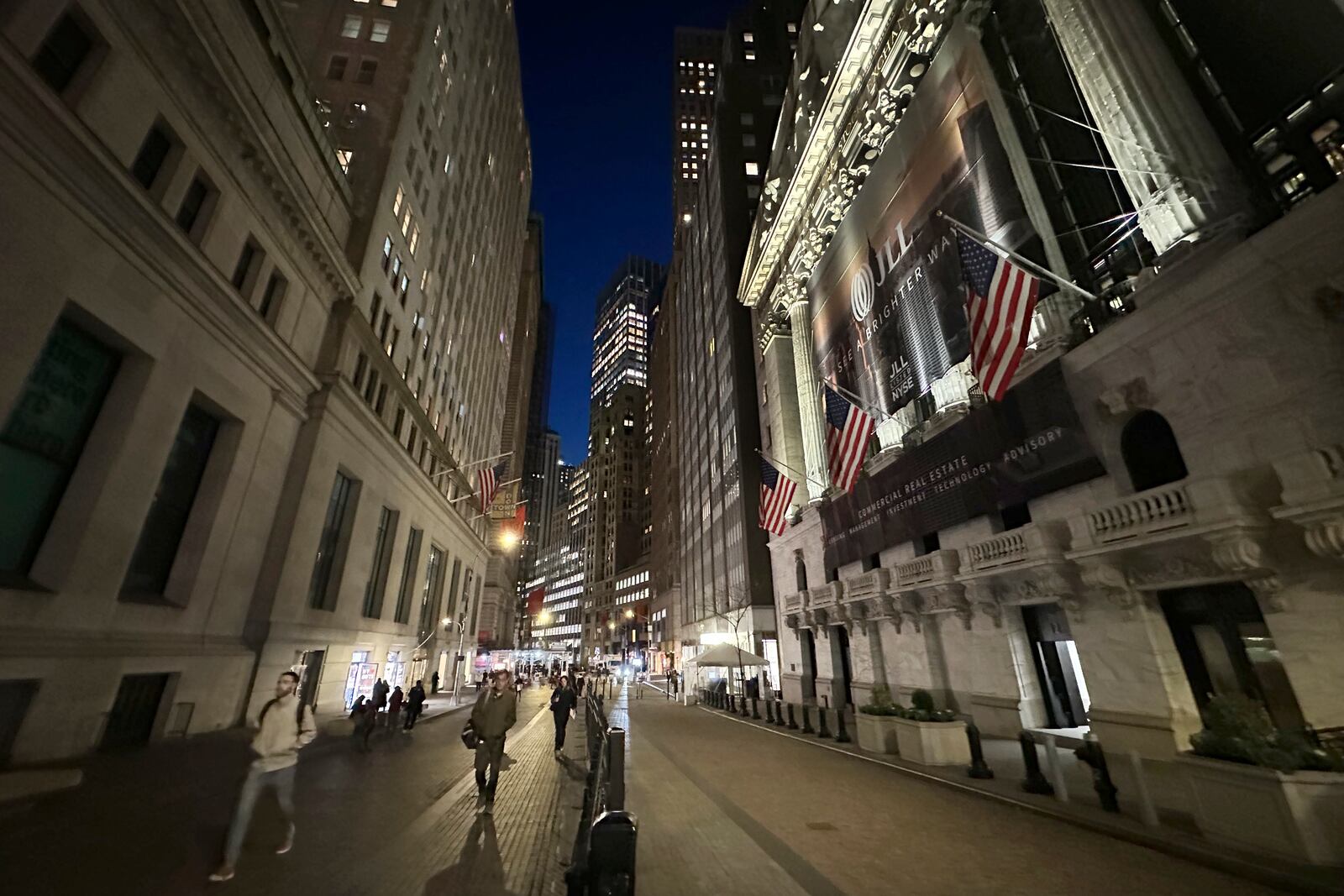 People pass the New York Stock Exchange, right, on Wednesday, Nov. 13, 2024, in New York. (AP Photo/Peter Morgan)