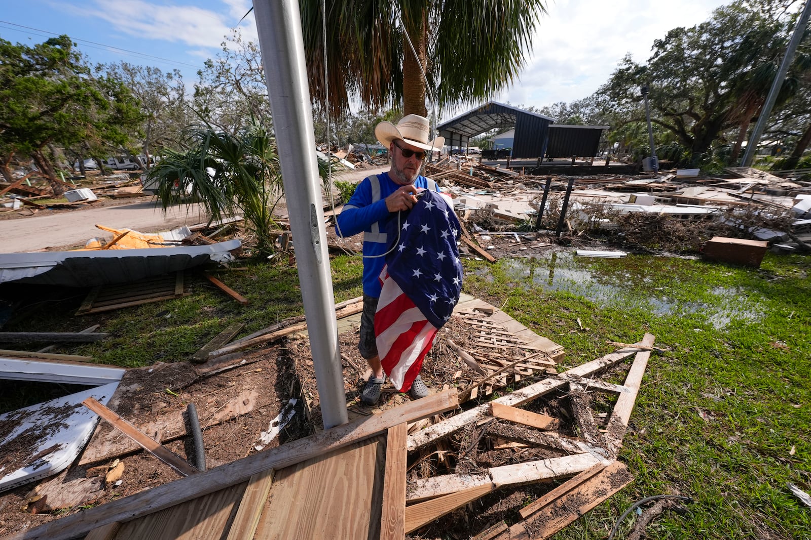 Chris Jordan, maintenance manager for Horseshoe Beach, hoists an American flag over the ruins of the city hall, in the aftermath of Hurricane Helene, in Horseshoe Beach, Fla., Saturday, Sept. 28, 2024. (AP Photo/Gerald Herbert)