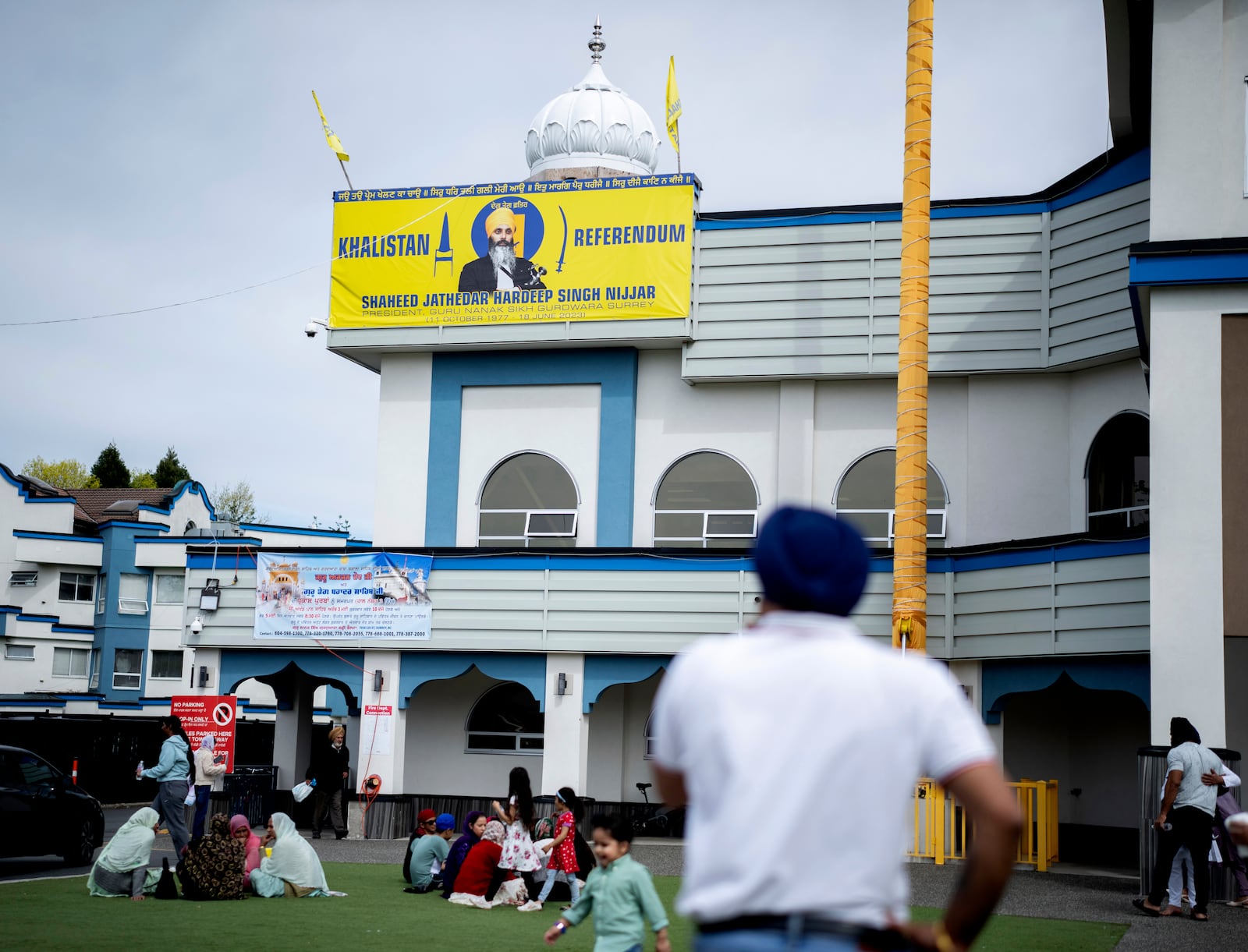 FILE -People sit on the lawn of the the Guru Nanak Sikh Gurdwara, below a picture of Hardeep Singh Nijjar in Surrey, B.C. on Friday, May 3, 2024. (Ethan Cairns/The Canadian Press via AP, File)