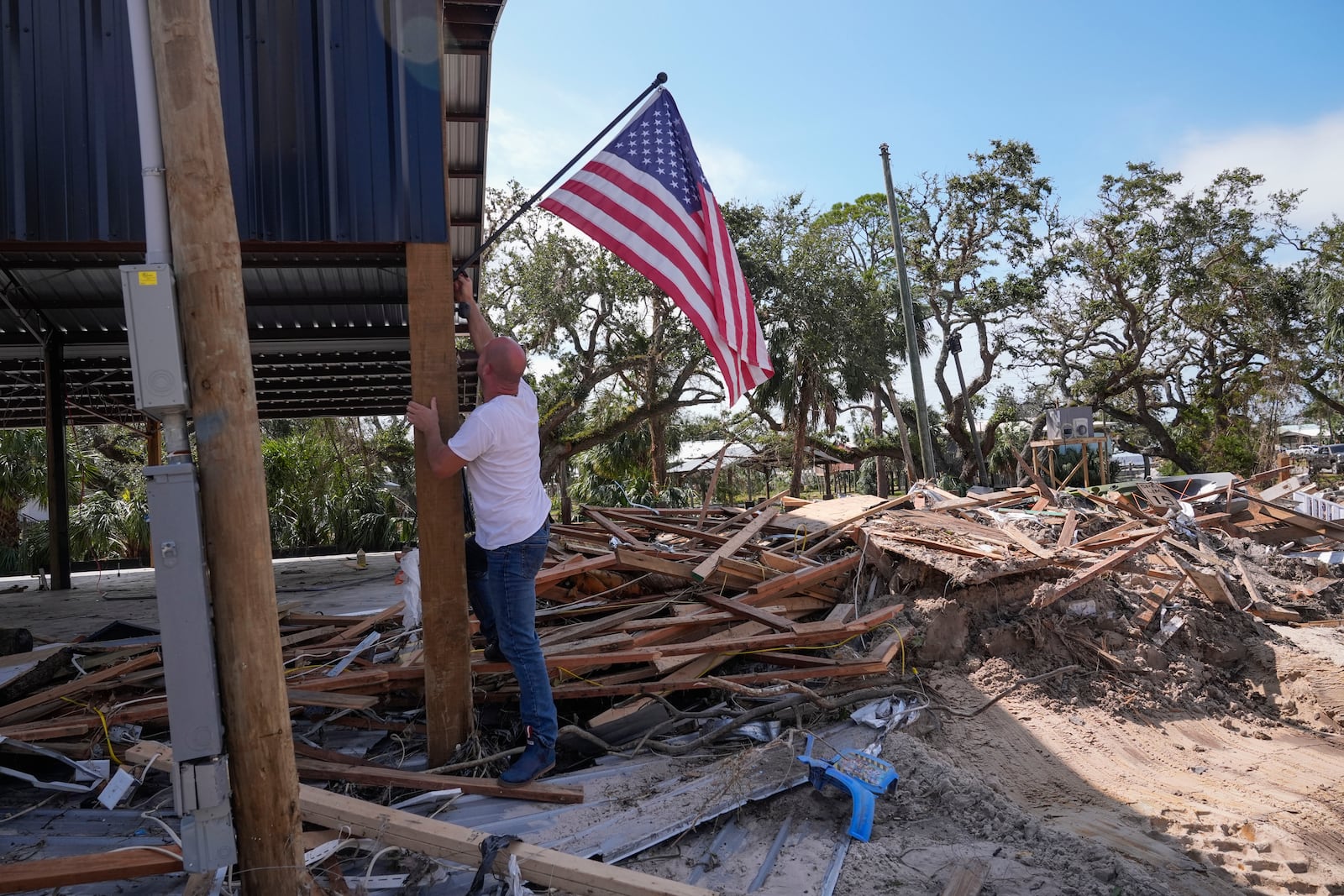 John Taylor puts up an American flag on his destroyed property in the aftermath of Hurricane Helene, in Horseshoe Beach, Fla., Saturday, Sept. 28, 2024. (AP Photo/Gerald Herbert)