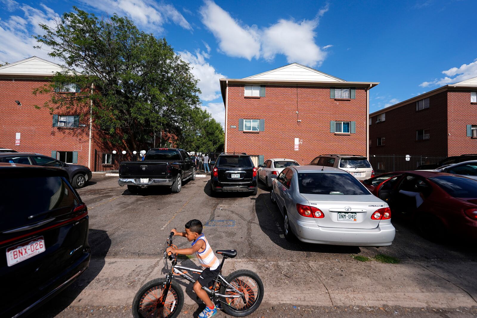 FILE - A boy guides his bicycle past apartment buildings as a rally organized by the East Colfax Community Collective is held in the courtyard to address chronic problems in the apartments occupied by people displaced from their home countries in central and South America, Tuesday, Sept. 3, 2024, in Aurora, Colo. (AP Photo/David Zalubowski, File)