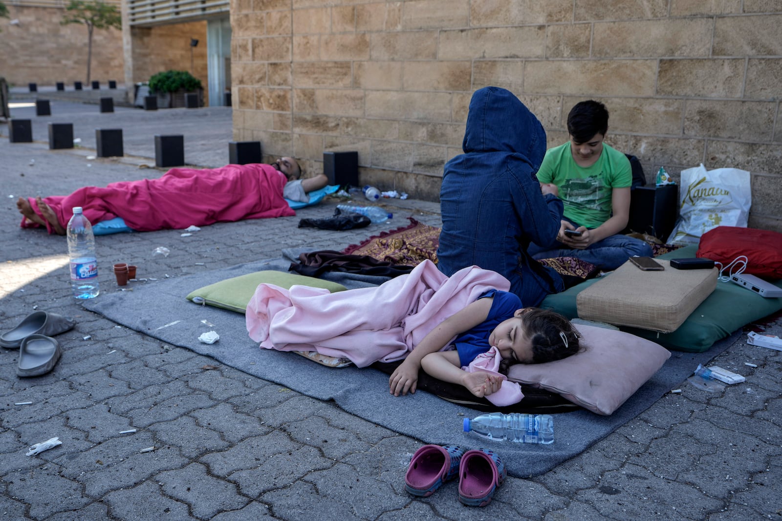 A family sleep on the ground in Beirut's corniche area after fleeing the Israeli airstrikes in the southern suburbs of Dahiyeh, Sunday, Sept. 29, 2024. (AP Photo/Bilal Hussein)