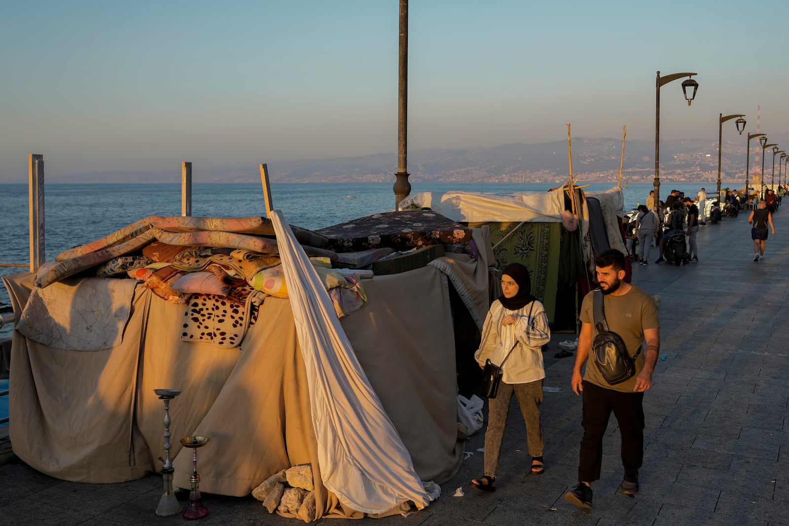 People walk past tents set up as temporary shelters by displaced families fleeing the Israeli airstrikes in the south and Dahiyeh, on Beirut's corniche, Lebanon, Tuesday Oct. 8, 2024. (AP Photo/Bilal Hussein)