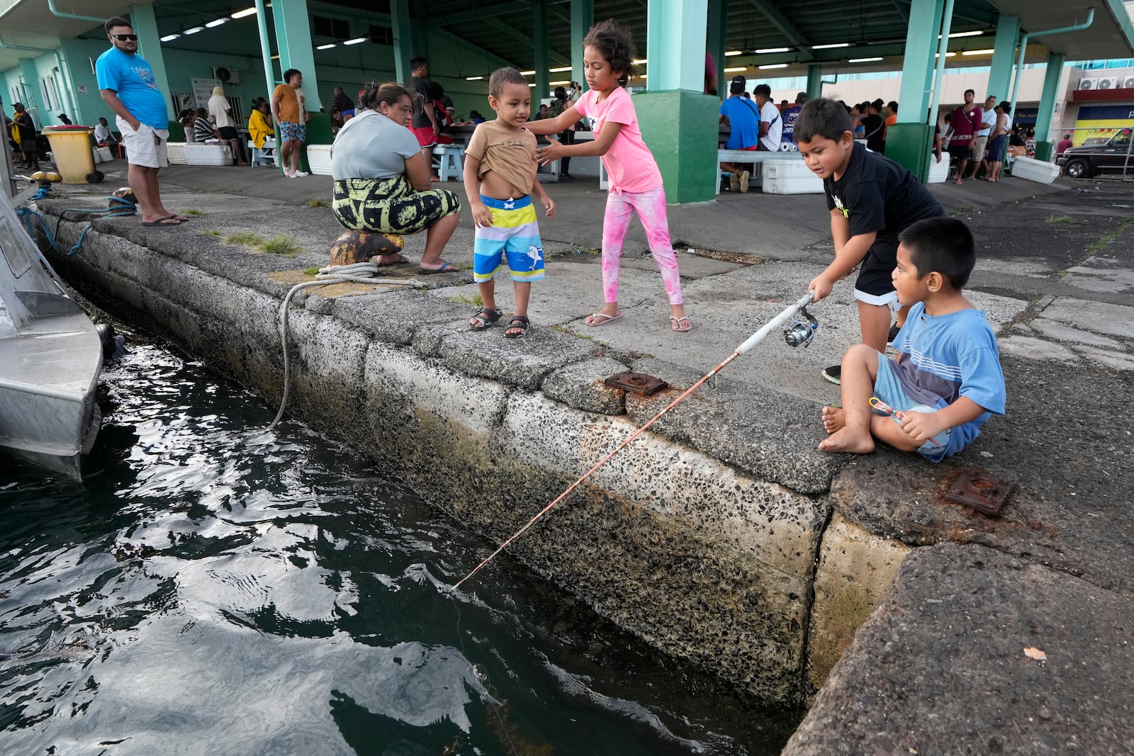 Children try their luck fishing off a dock next to a fish market in Apia, Samoa, on Sunday, Oct. 20, 2024. (AP Photo/Rick Rycroft)