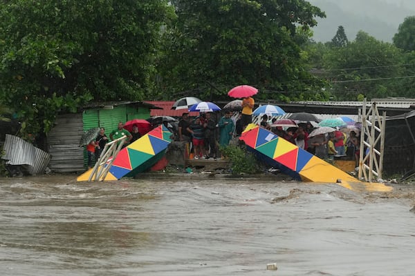 People stand at a pedestrian bridge collapsed due to flooding caused by rains brought on by Tropical Storm Sara in San Pedro Sula, Honduras Saturday, Nov. 16, 2024. (AP Photo/Moises Castillo)