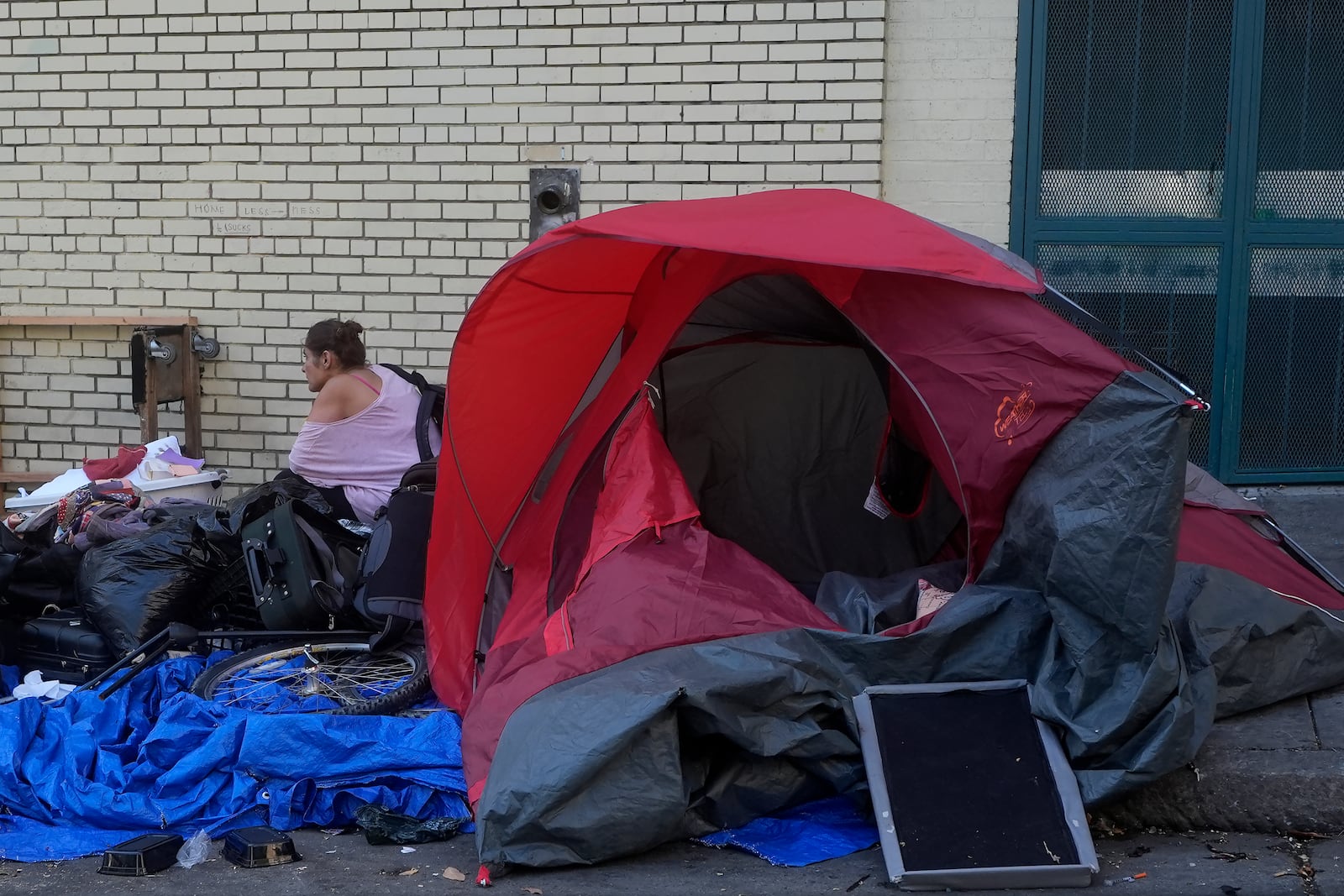 A person sits behind a tent on a sidewalk in San Francisco, Thursday, Aug. 29, 2024. (AP Photo/Jeff Chiu)