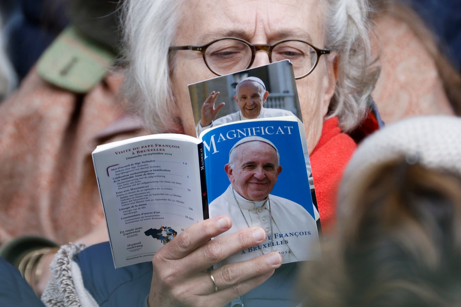 A faithful reads a book as Pope Francis presides the holy mass, at the King Baudouin stadium in Brussels, Belgium, Sunday, Sept. 29, 2024. (AP Photo/Omar Havana)