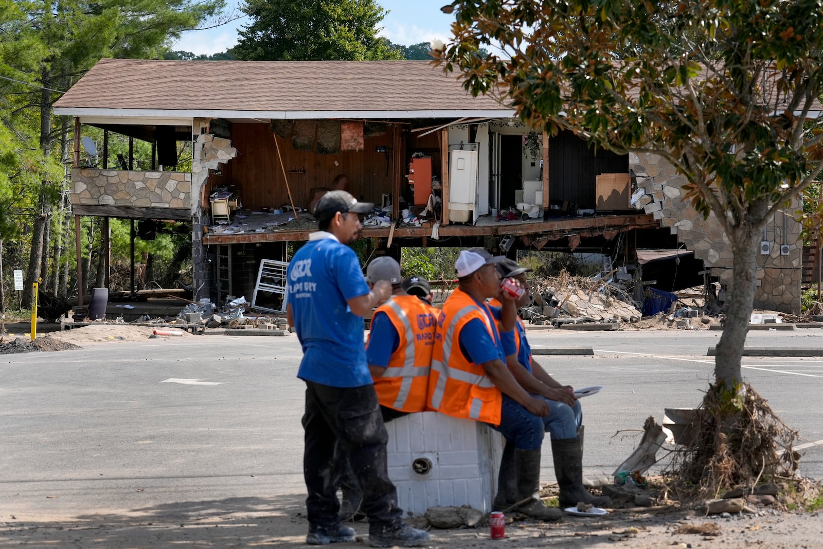 Workers helping with clean up efforts stop for lunch under the shade of a tree as a building destroyed by Hurricane Helene is seen in the background Saturday, Oct. 5, 2024, in Newport, Tenn. (AP Photo/Jeff Roberson)