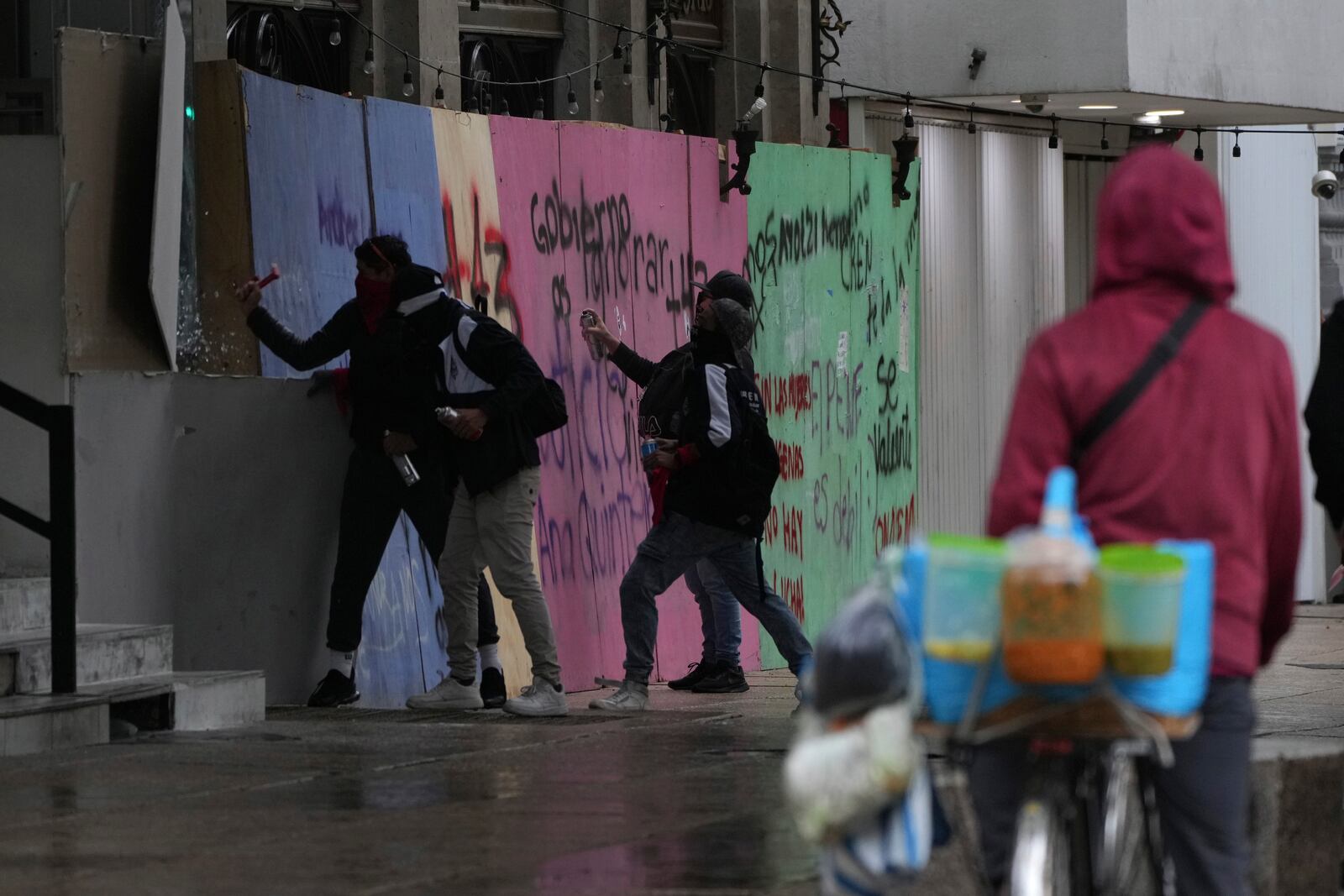 Masked youths crack a window as others spray paint anti-government slogans on a barrier protecting a storefront restaurant during a march marking the 10-year anniversary of the disappearance of 43 students from an Ayotzinapa rural teacher's college, in Mexico City, Thursday, Sept. 26, 2024. (AP Photo/Fernando Llano)