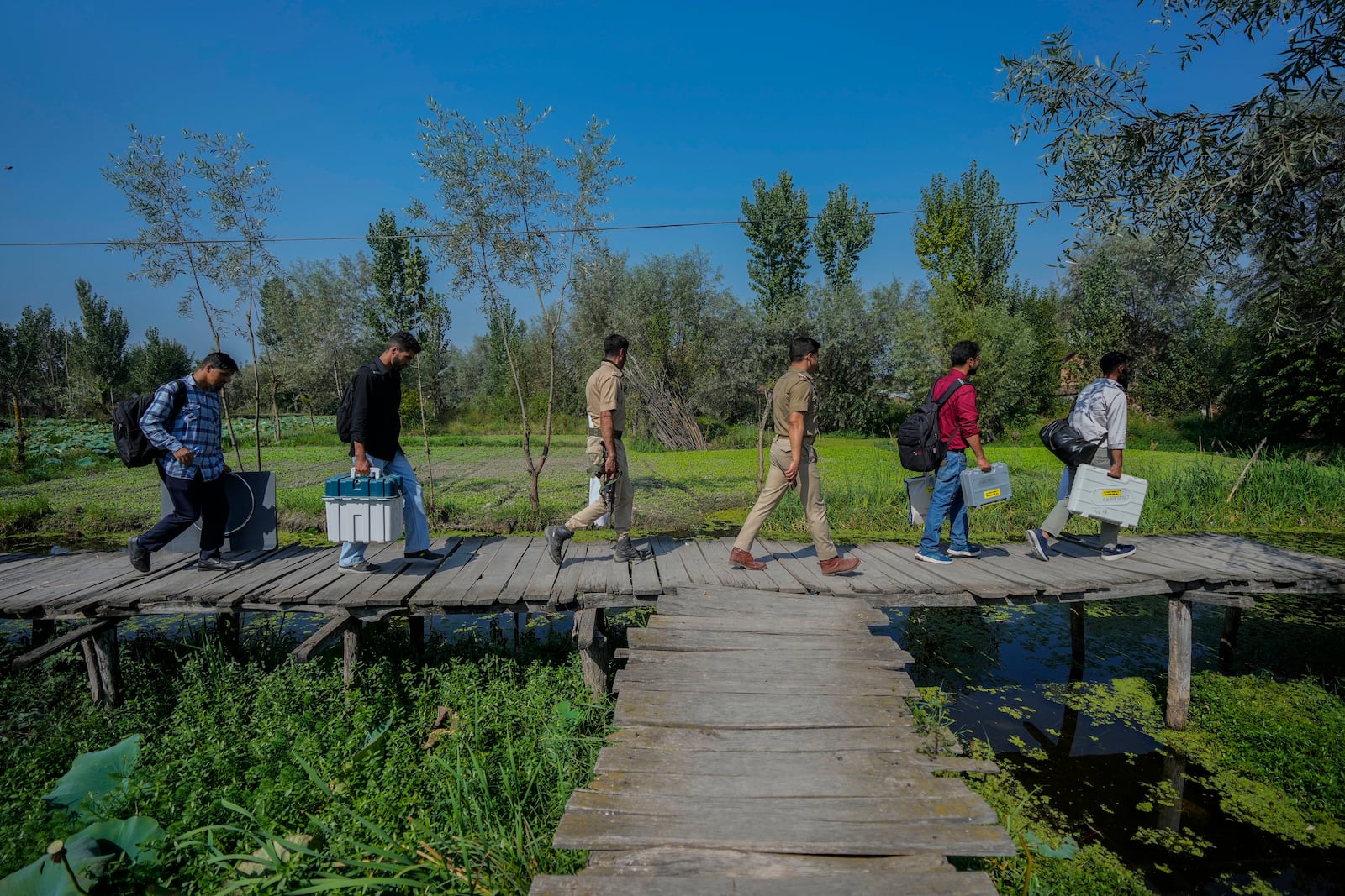 Polling officials and police walk on a wooden bridge towards a polling station in the interior of Dal Lake ahead of the second phase of voting for choosing a local government in Indian-controlled Kashmir, in Srinagar, Tuesday, Sept. 24, 2024. (AP Photo/Mukhtar Khan)