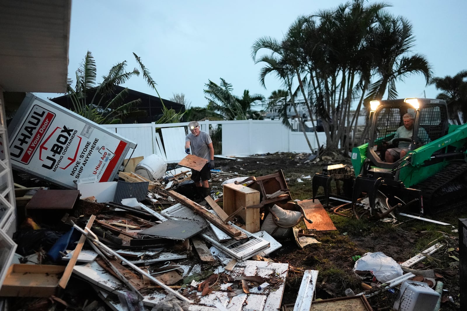 Homeowner Robert Turick, 68, left, and storm waste removal contractor Sven Barnes work to clear debris that Hurricane Milton storm surge swept from other properties into Turick's canal-facing back yard, in Englewood, Fla., Friday, Oct. 11, 2024. Turick, whose family has owned the home for more than 25 years, said it had never flooded until 2022's Hurricane Ian, but since then, it has flooded in three more hurricanes, each bringing higher water levels than the last. (AP Photo/Rebecca Blackwell)