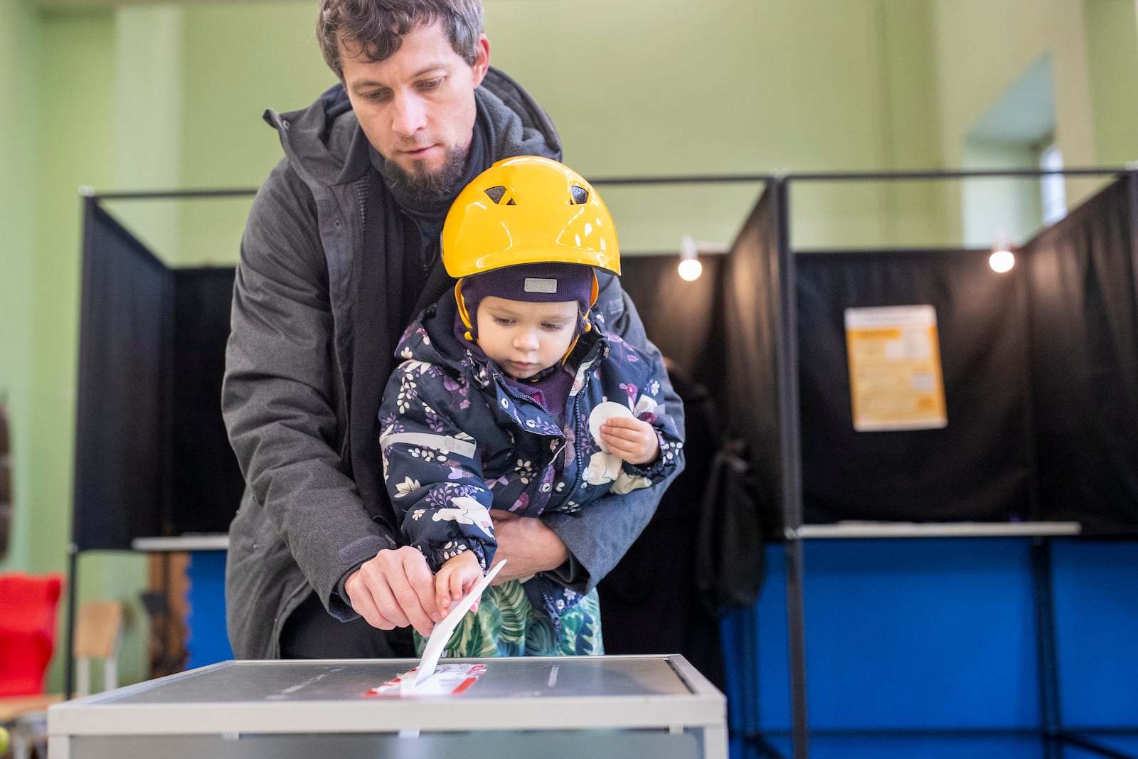 A man with a child casts his ballot at a polling station during the first round of voting in parliamentary elections, in Vilnius, Lithuania, Sunday, Oct. 13, 2024. (AP Photo/Mindaugas Kulbis)