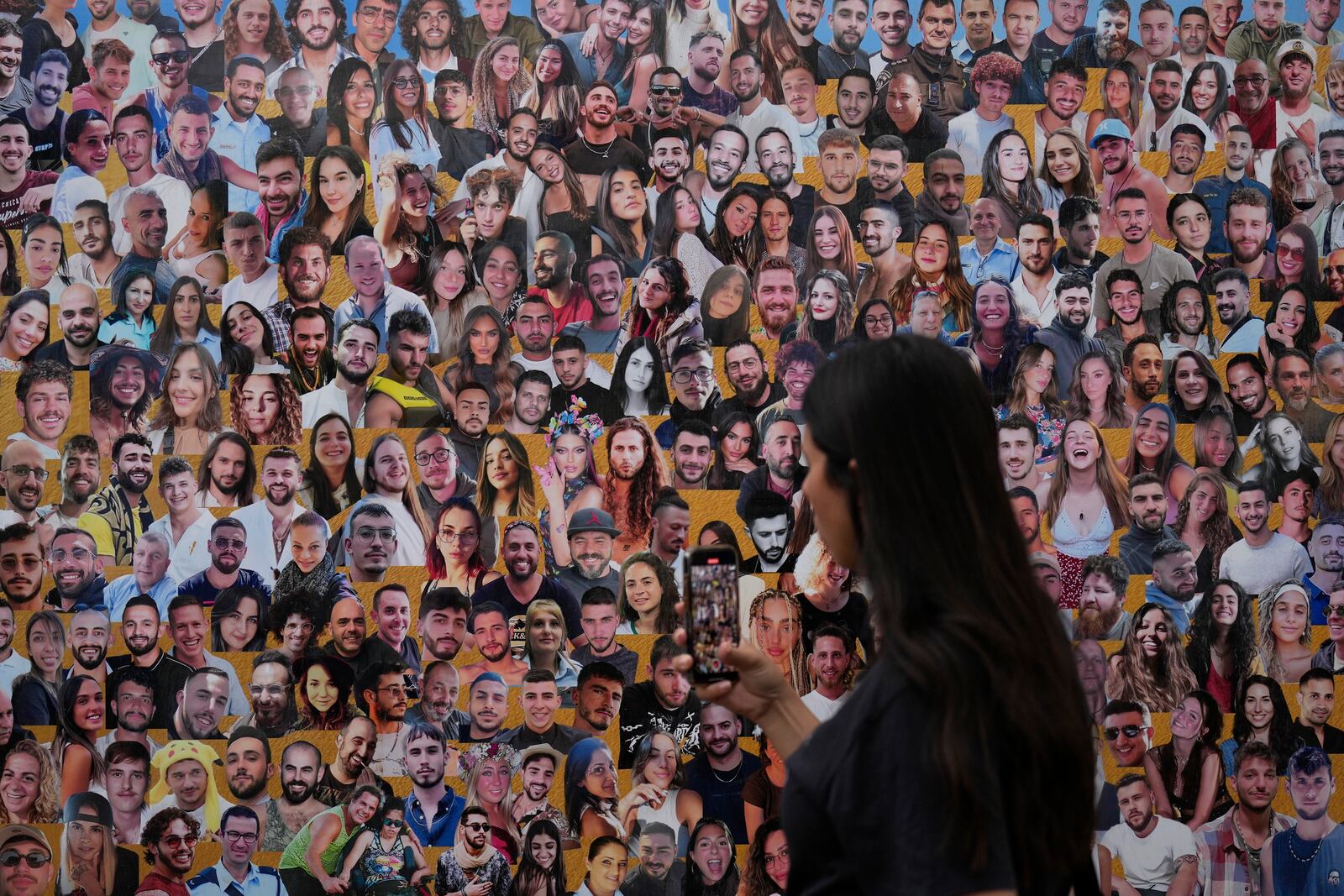 An attendant walks through a mural with portraits of the victims at the site of the Nova music festival, where hundreds of revelers were killed and abducted by Hamas and taken into Gaza, on the one-year anniversary of the attack, near Kibbutz Reim, southern Israel, Monday, Oct. 7, 2024. (AP Photo/Ariel Shalit)