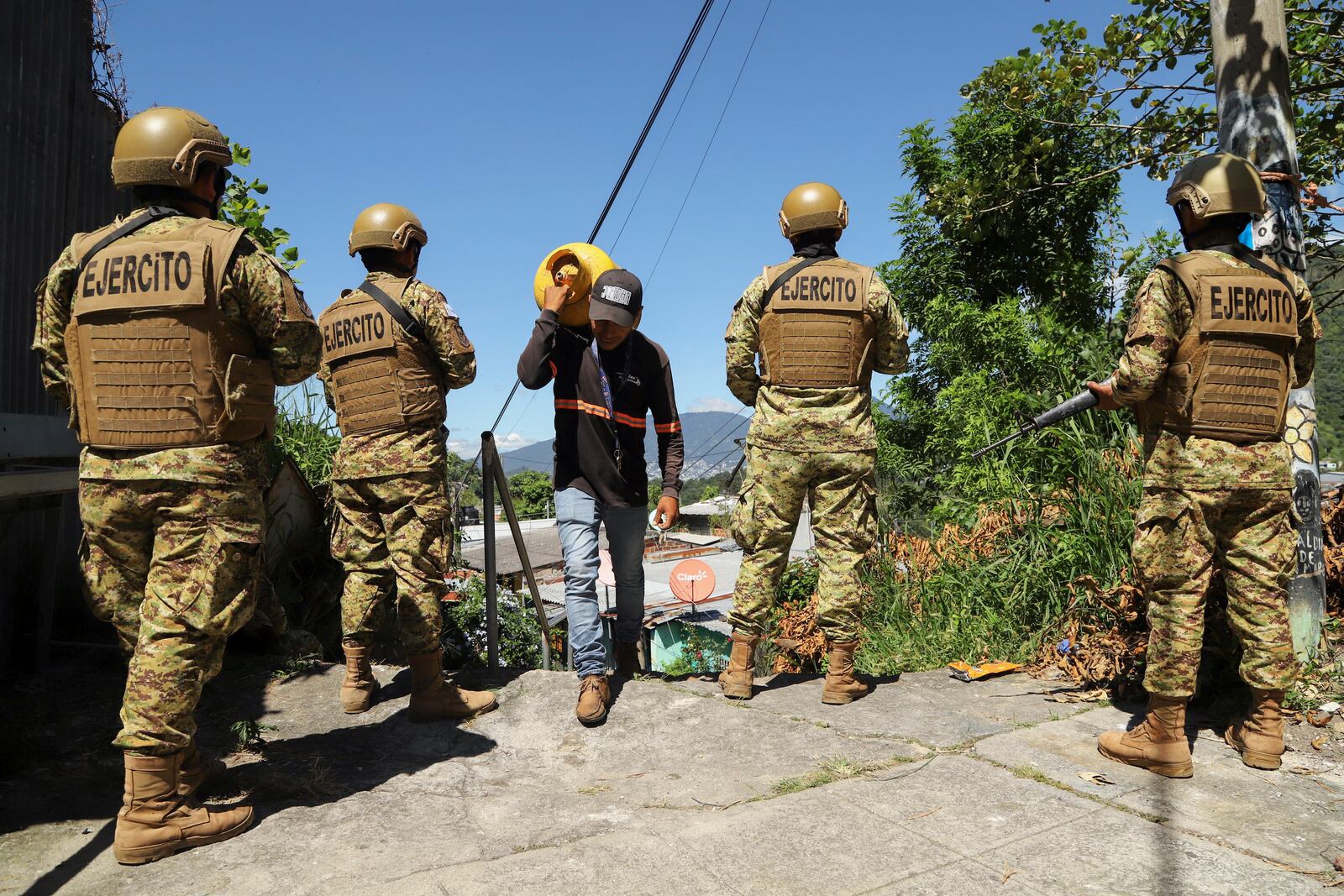 A man carries propane past soldiers in the 10 de Octubre neighborhood during a government deployment of soldiers and police to crack down on gangs in San Marcos, El Salvador, Monday, Oct. 28, 2024. (AP Photo/Salvador Melendez)