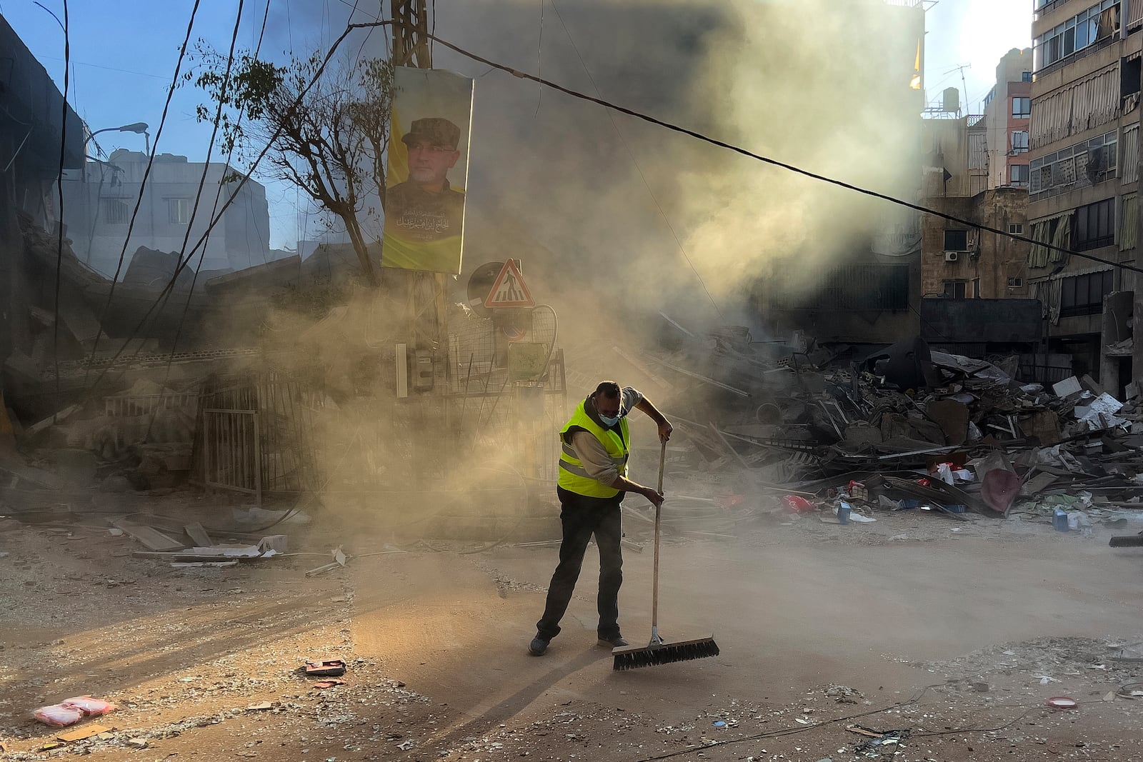 A worker cleans a street as smoke rises from a destroyed building that was hit by an Israeli airstrike in Dahiyeh, in the southern suburb of Beirut, Lebanon, early Sunday, Oct. 20, 2024. (AP Photo/Hussein Malla)