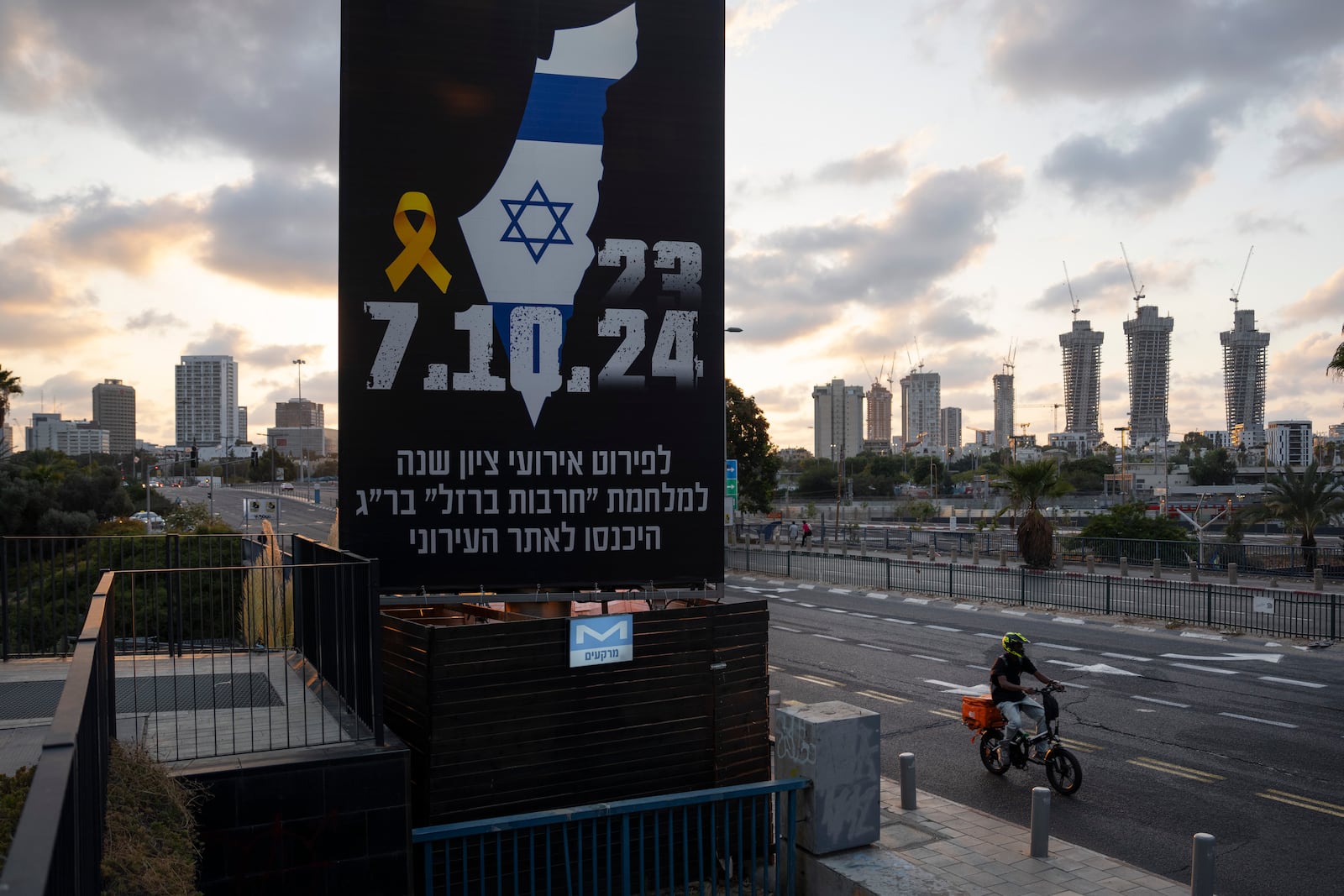 A man rides his bicycle next to a billboard with information about upcoming events marking the one-year anniversary of the Oct. 7 Hamas attack on Israel, in Tel Aviv, Israel, on Saturday, Oct. 5, 2024. (AP Photo/Oded Balilty)